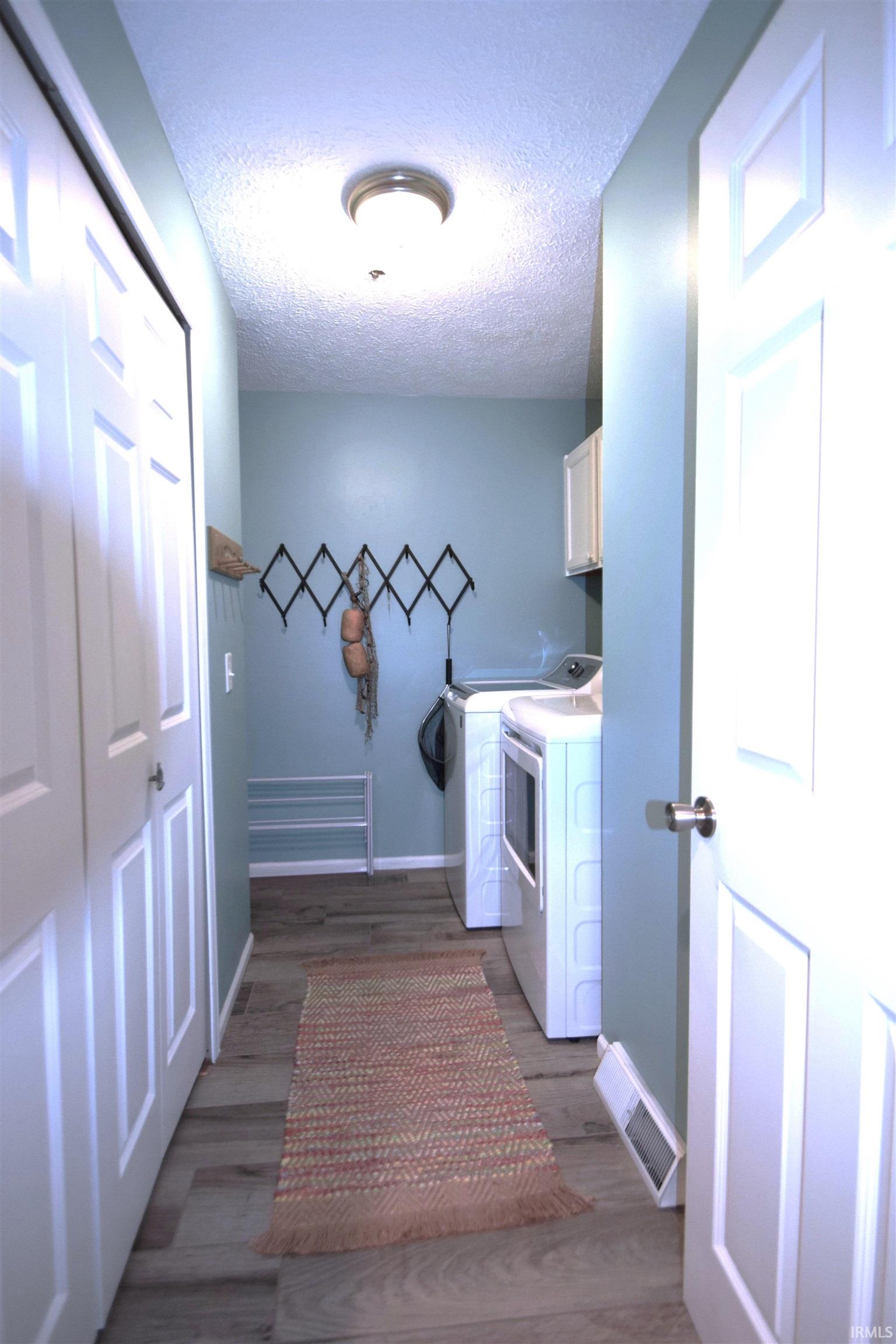 Laundry area featuring dark wood-style floors, a textured ceiling, cabinet space, and washer and clothes dryer