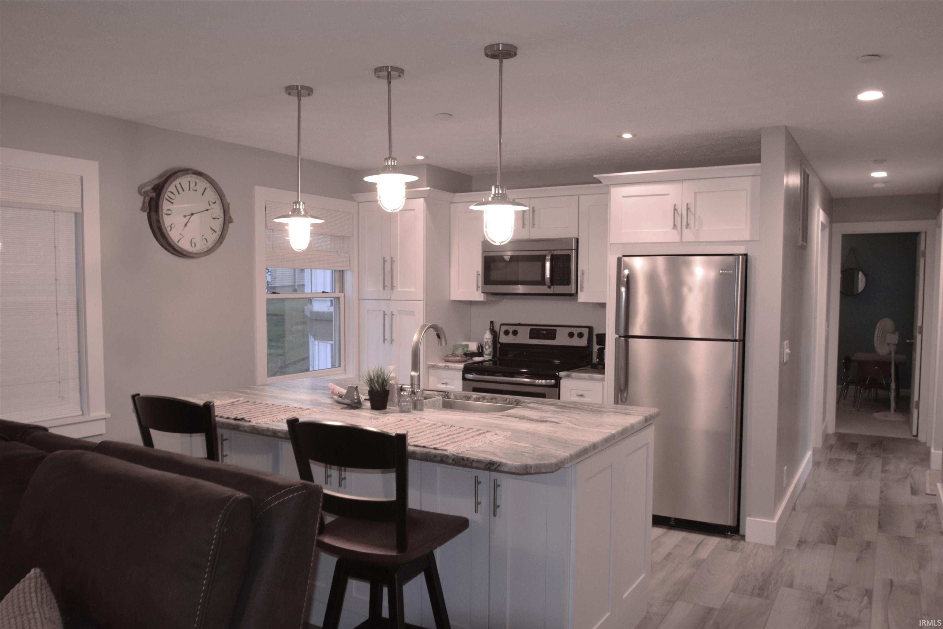 Kitchen featuring a kitchen breakfast bar, stainless steel appliances, white cabinets, an island with sink, and light stone countertops