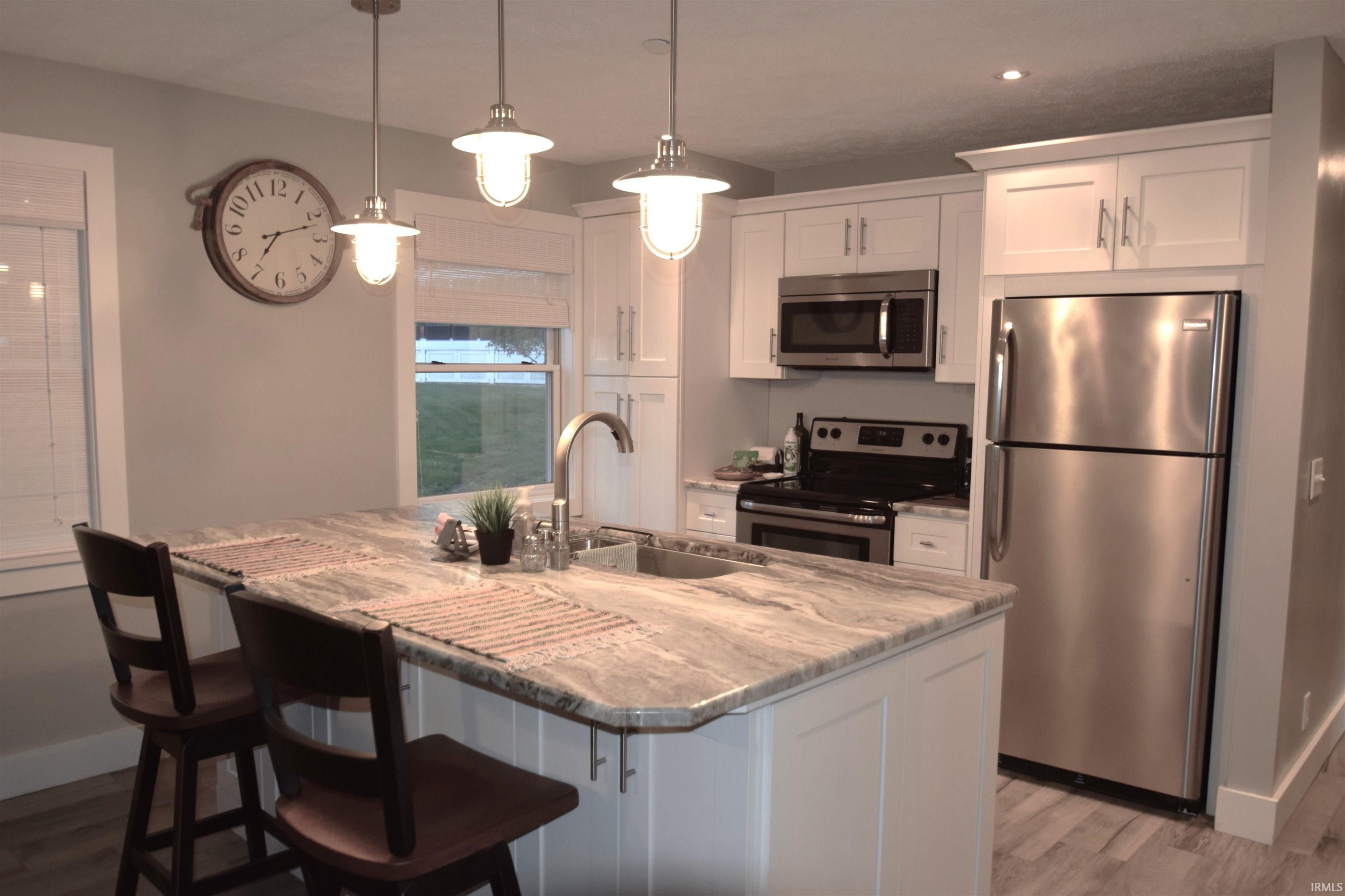 Kitchen with stainless steel appliances, white cabinetry, light stone counters, and a breakfast bar