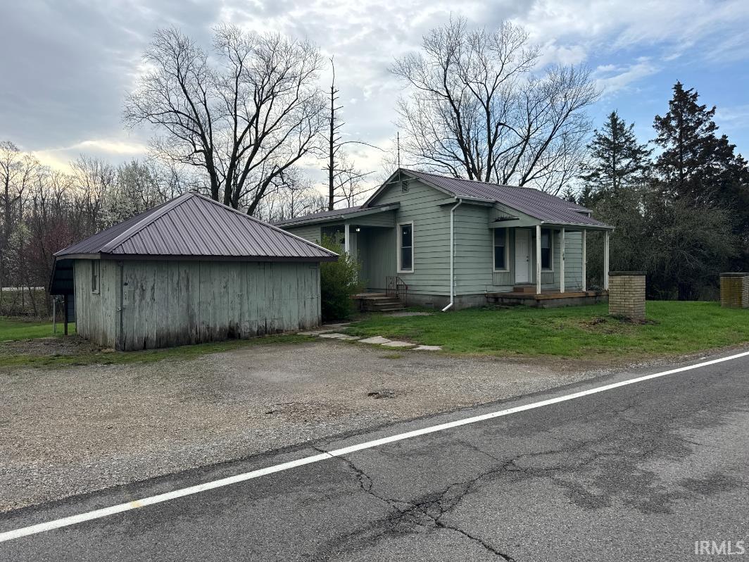 View of front of home featuring a front yard, a metal roof, an outbuilding, and covered porch