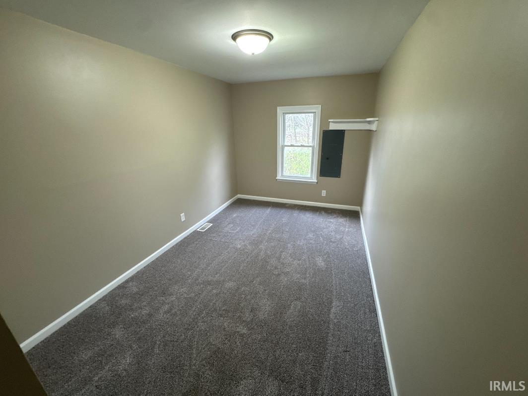 Unfurnished room featuring dark colored carpet and electric panel
