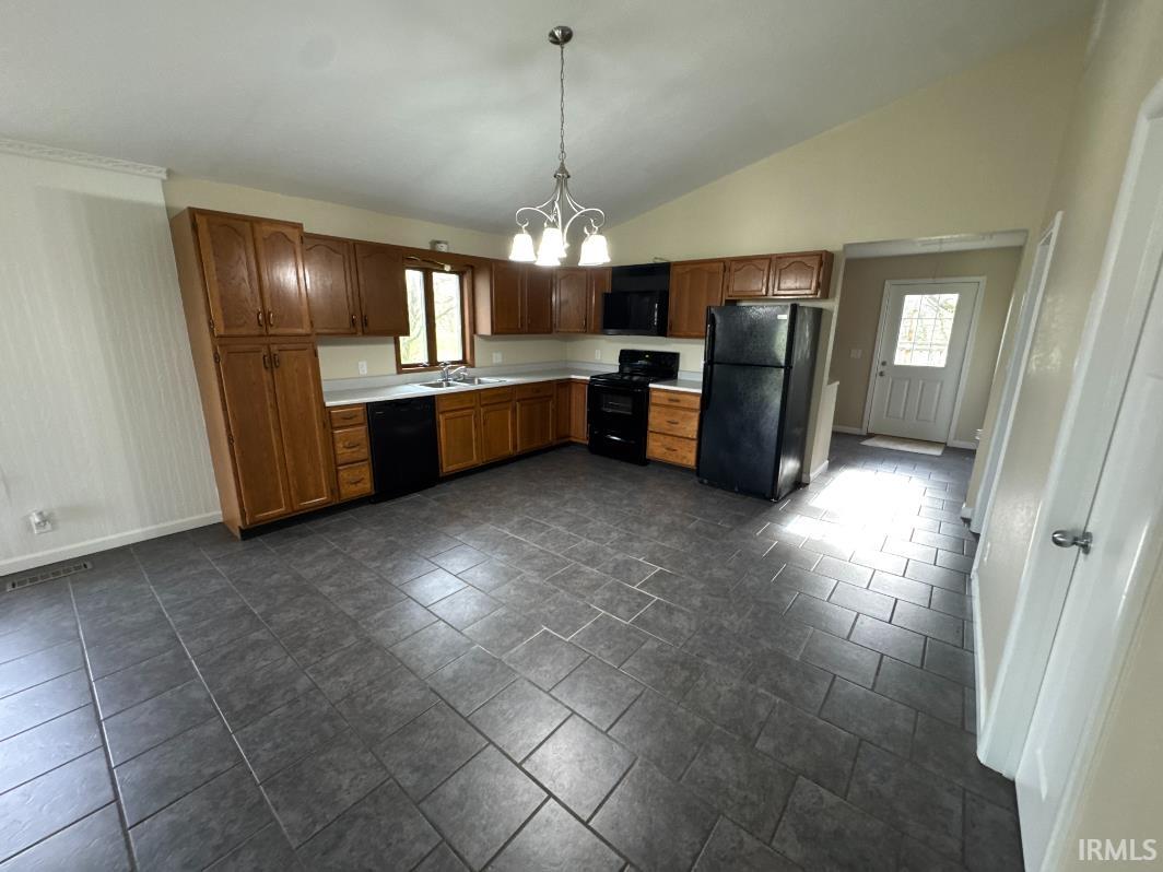 Kitchen featuring hanging lights, black appliances, light countertops, lofted ceiling, and wood finish cabinets