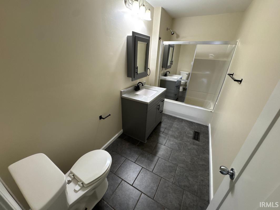 Full bath with vanity, shower / bath combination with glass door, and dark tile patterned floors