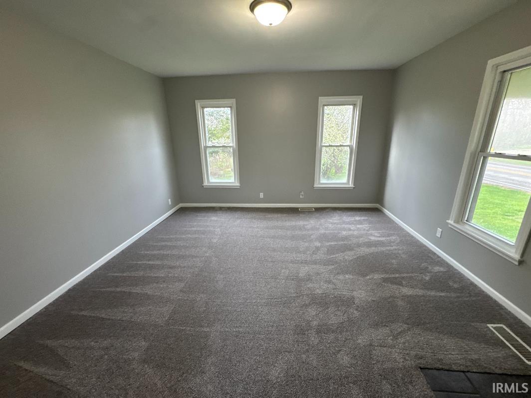 Empty room featuring baseboards and dark carpet
