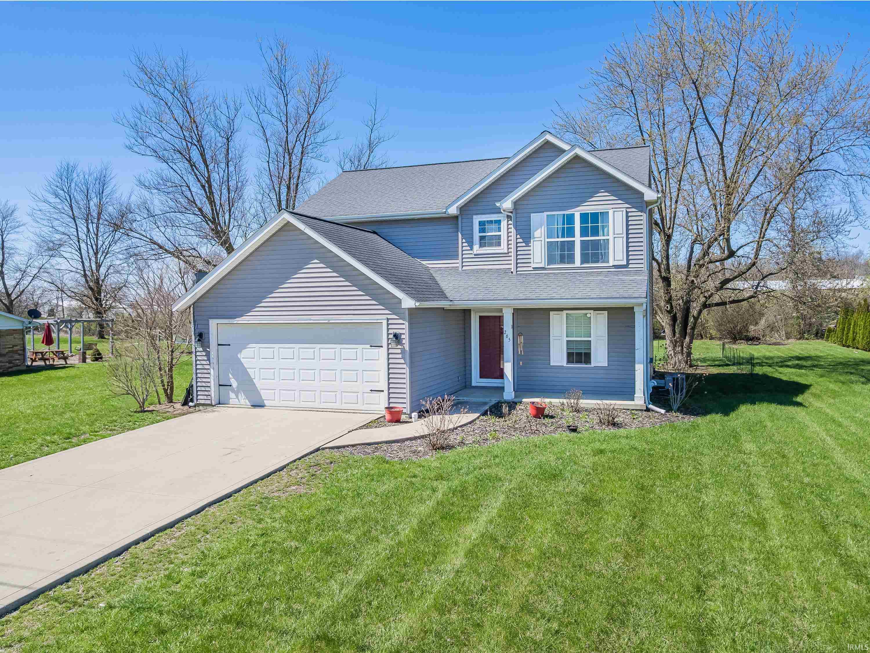Traditional-style home featuring a front yard, driveway, an attached garage, roof with shingles, and covered porch
