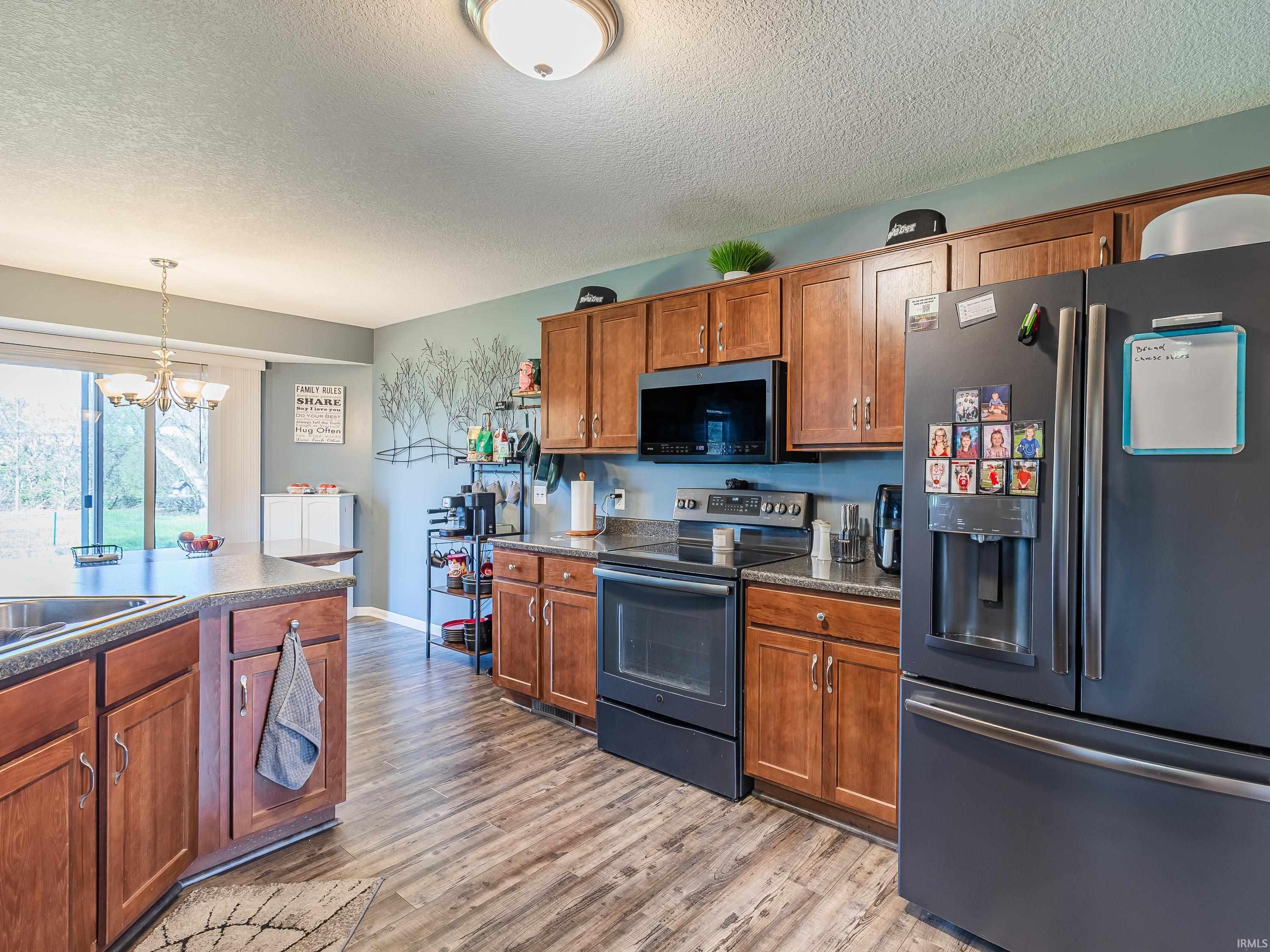 Kitchen featuring refrigerator with ice dispenser, black range with electric cooktop, wood finish cabinets, dark countertops, and a textured ceiling
