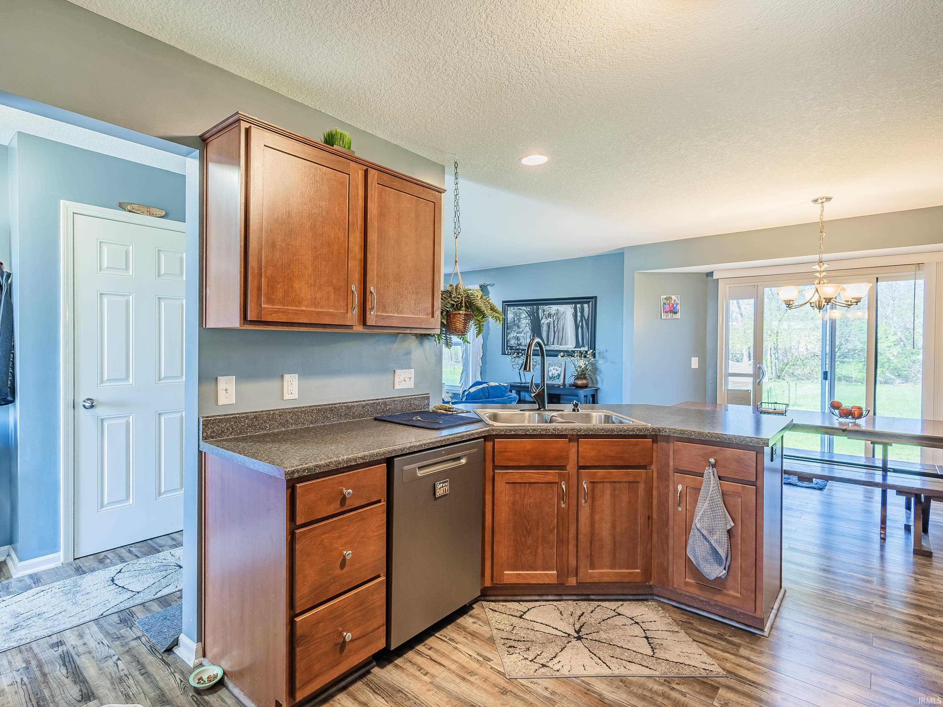 Kitchen featuring dark countertops, a peninsula, wood finish cabinets, a chandelier, and dishwasher