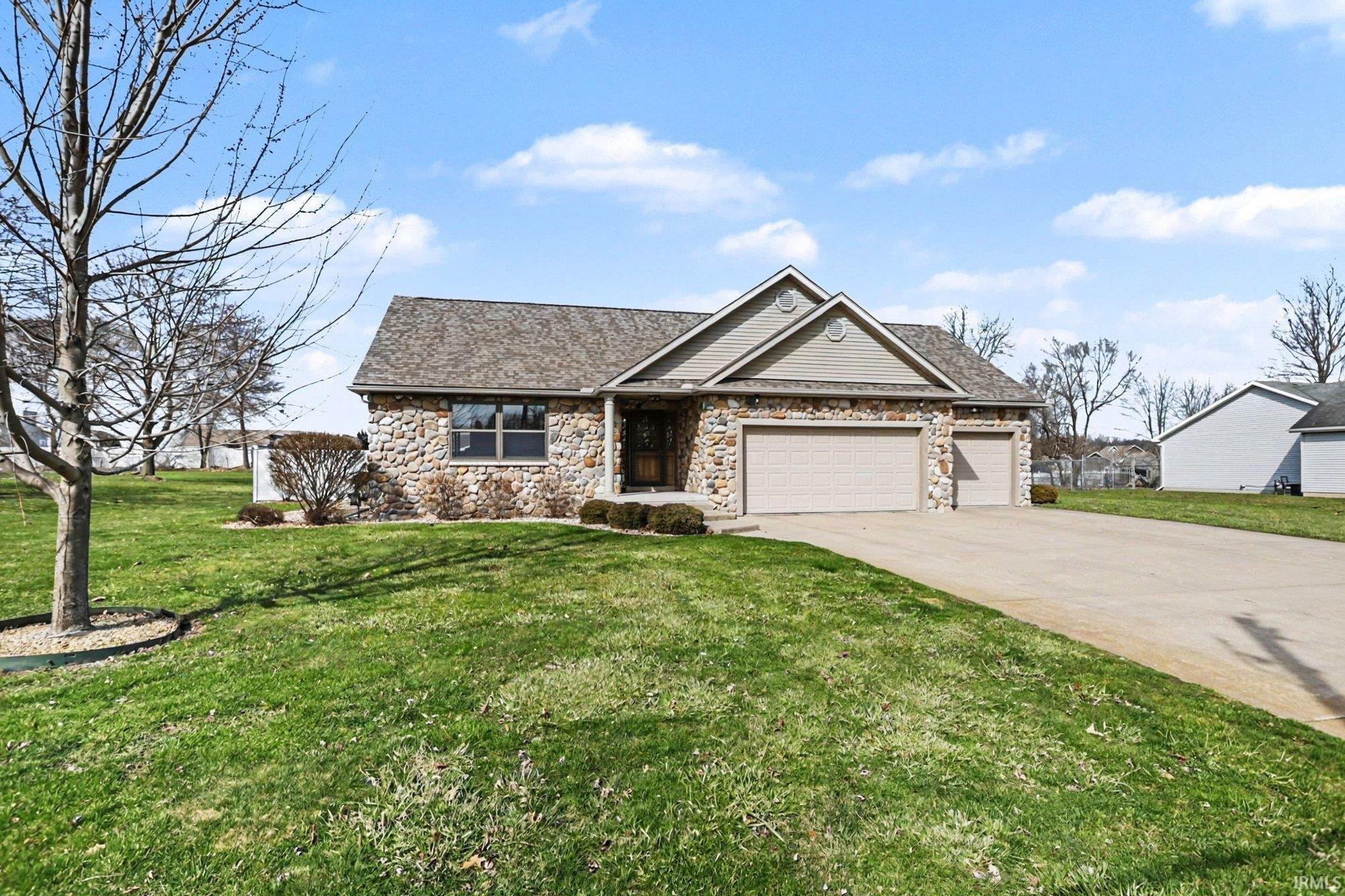 View of front of property with a front yard, a garage, concrete driveway, and stone siding