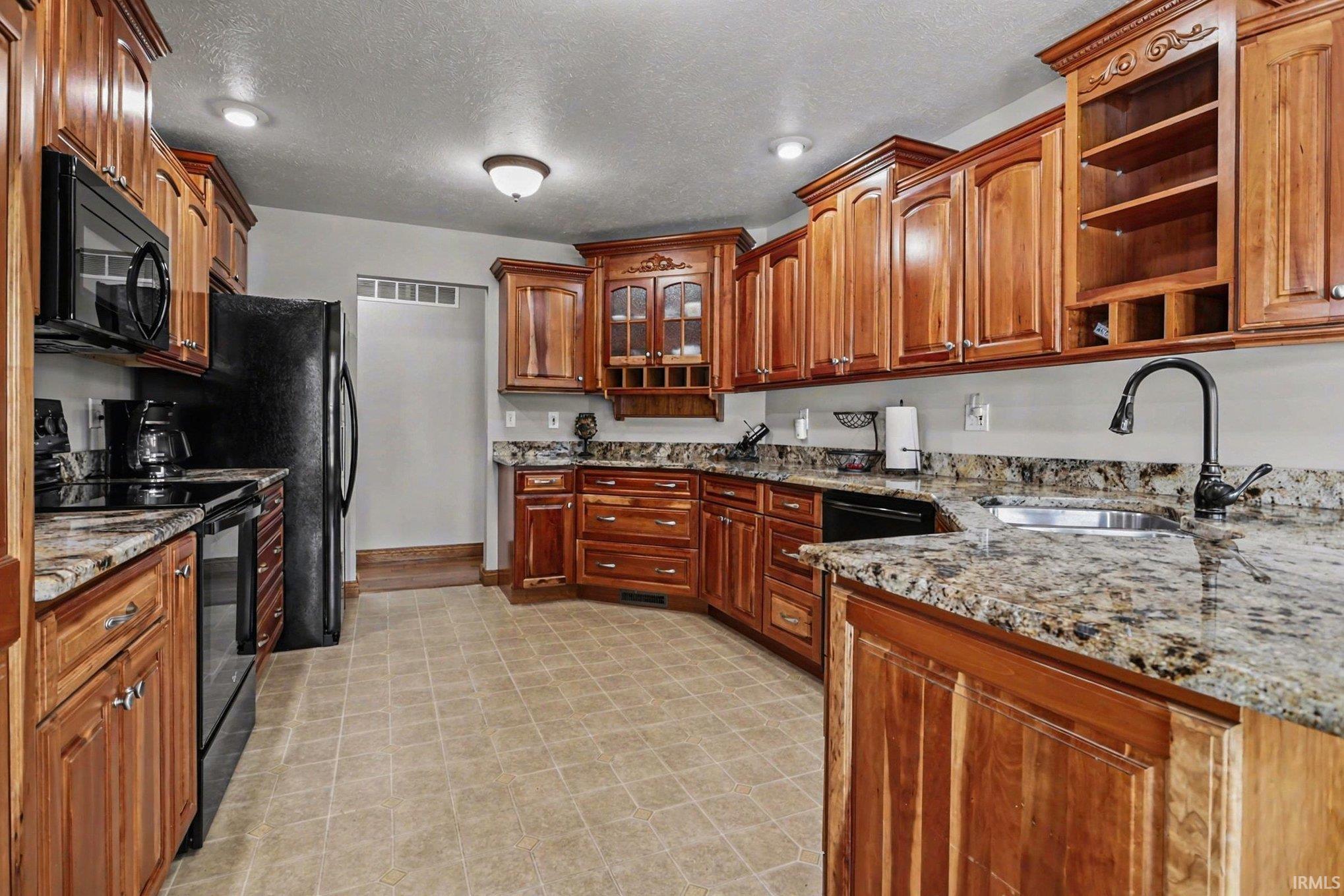 Kitchen with black appliances, dark stone countertops, open shelves, wood finish cabinetry, and a textured ceiling