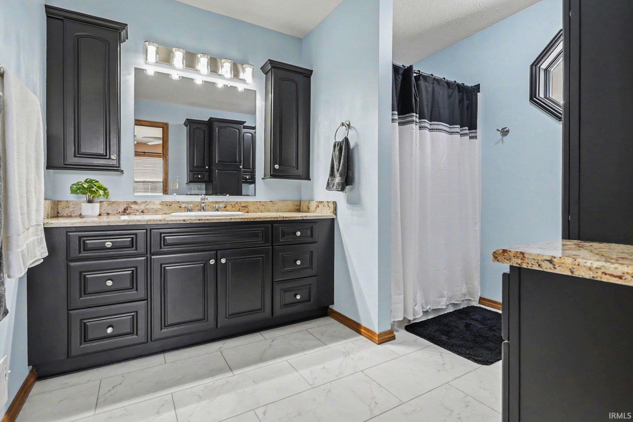 Bathroom featuring light marble finish floors, vanity, and a shower stall