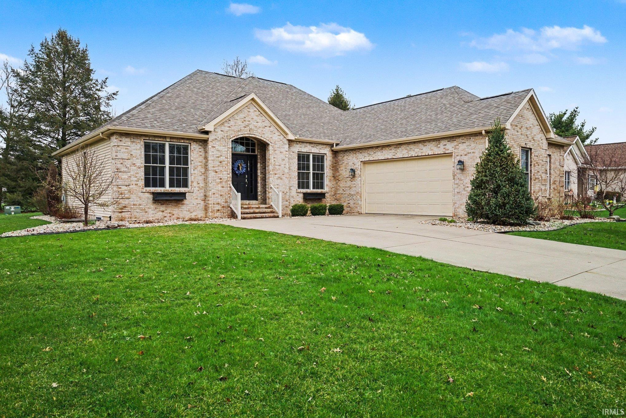 View of front facade featuring brick siding, roof with shingles, a garage, and a front yard