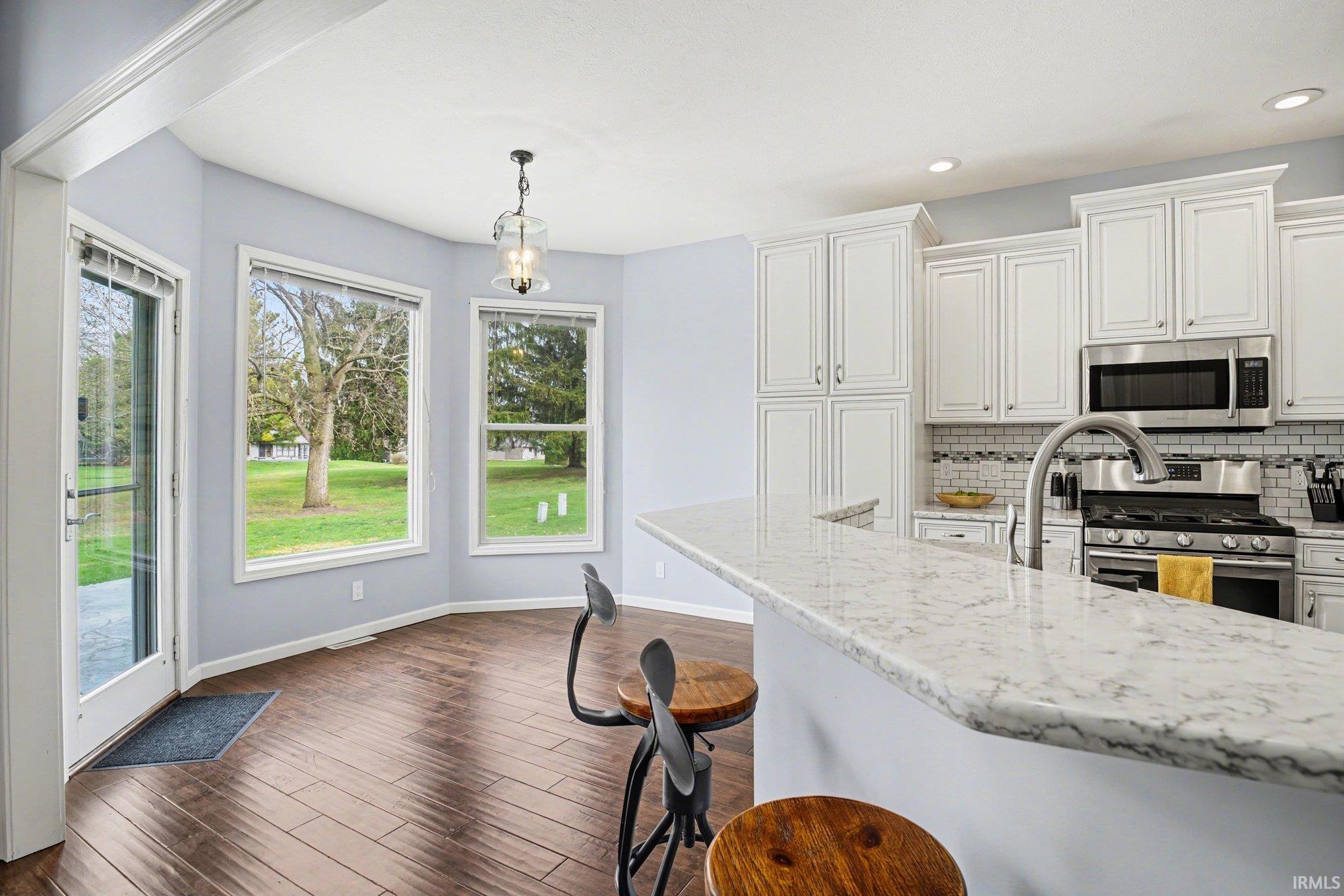 Kitchen with stainless steel appliances, white cabinetry, light stone counters, hanging light fixtures, and backsplash