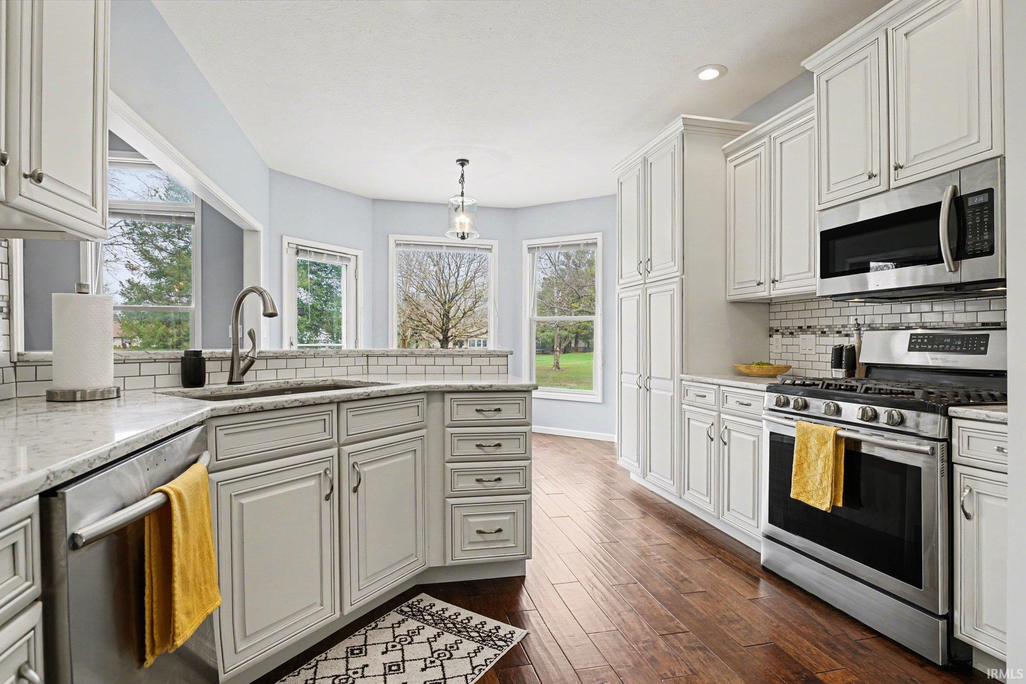 Kitchen with stainless steel appliances, backsplash, light stone countertops, pendant lighting, and white cabinets