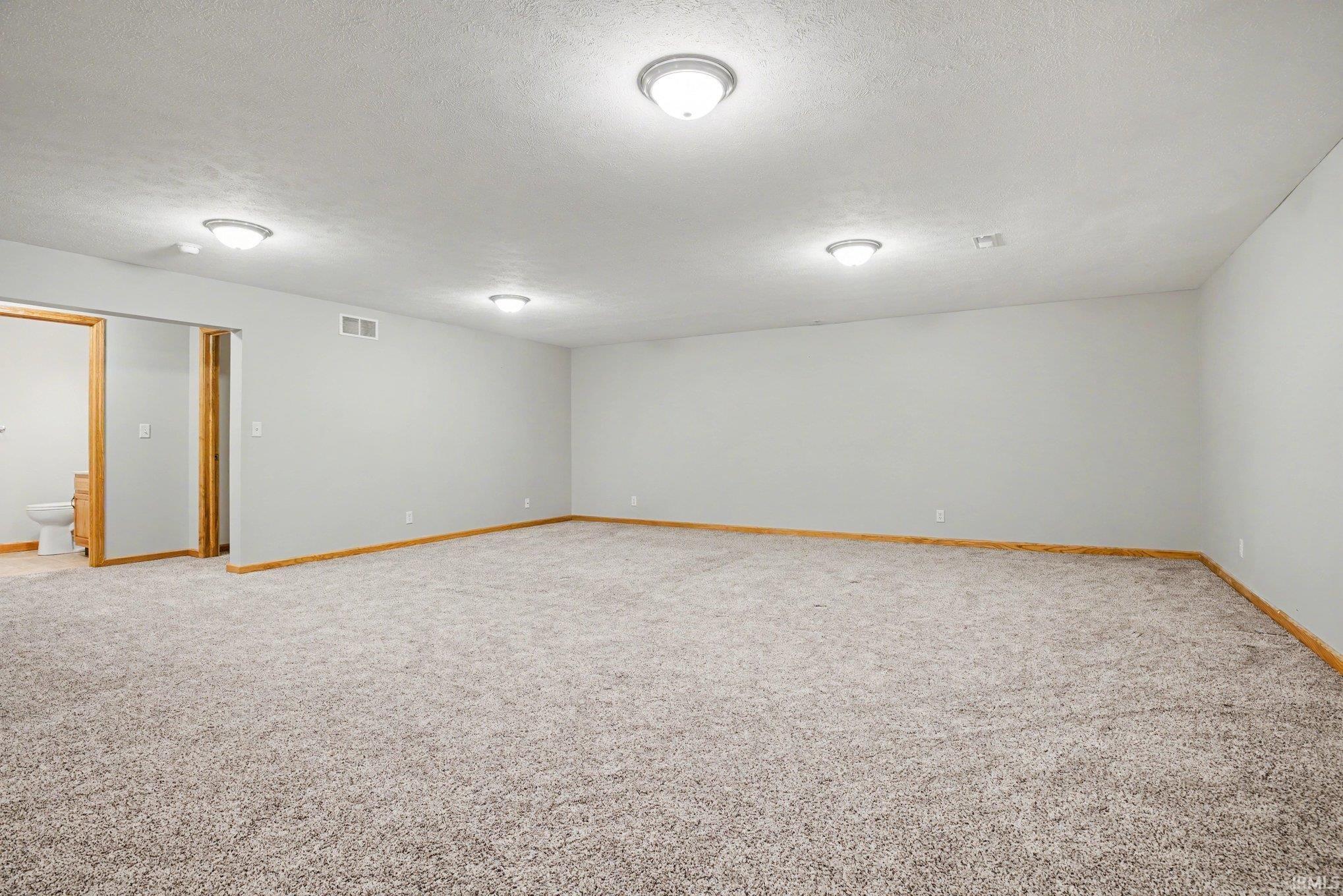 Empty room with light colored carpet and a textured ceiling