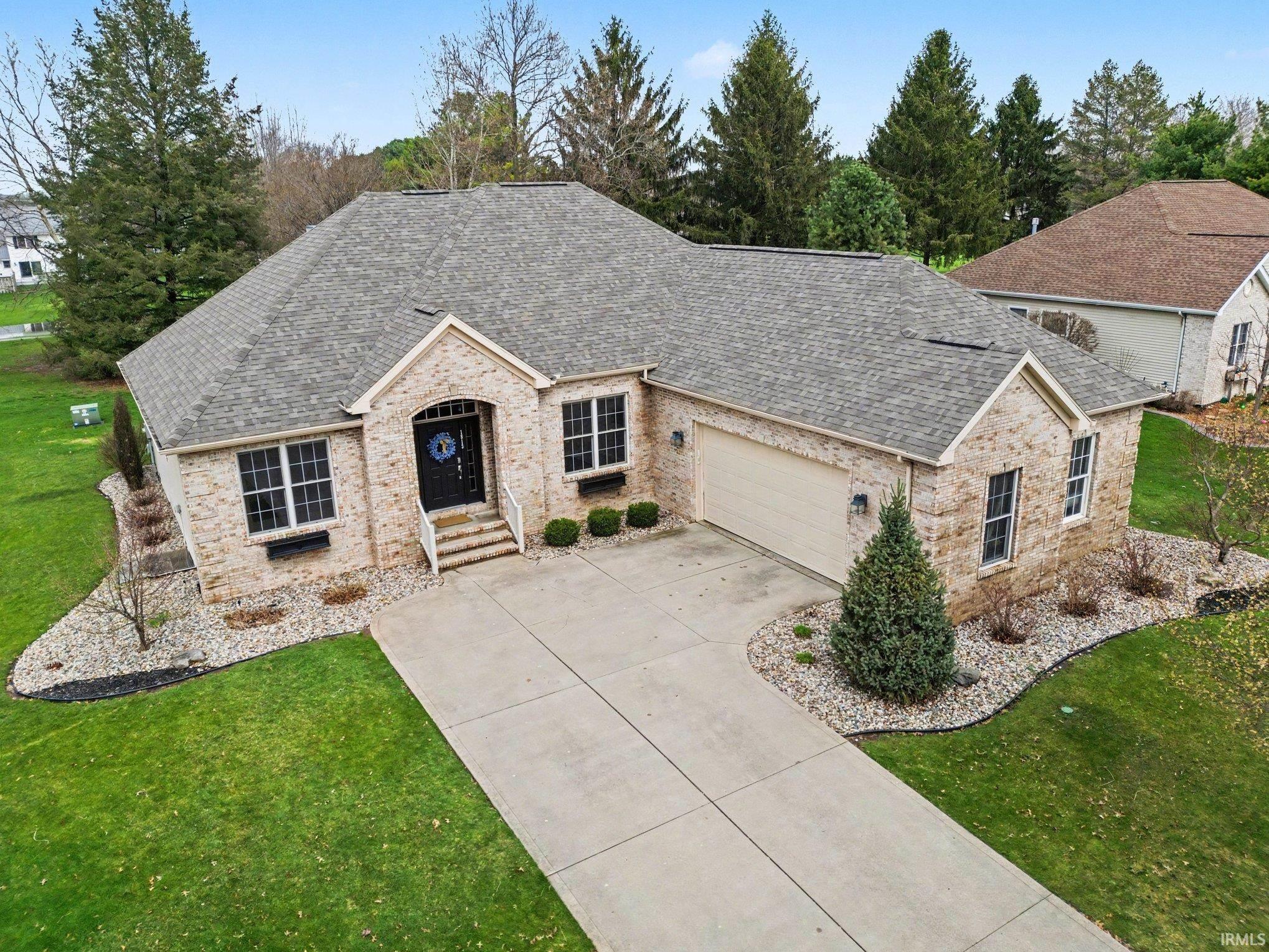 Ranch-style home with a garage, roof with shingles, a front lawn, brick siding, and driveway