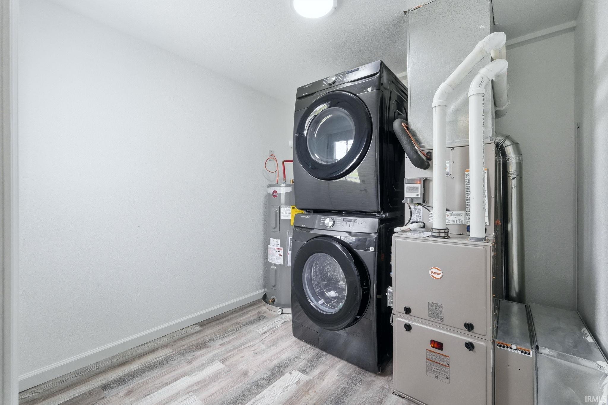 Laundry area with light wood-style floors, electric water heater, stacked washer / dryer, and heating unit