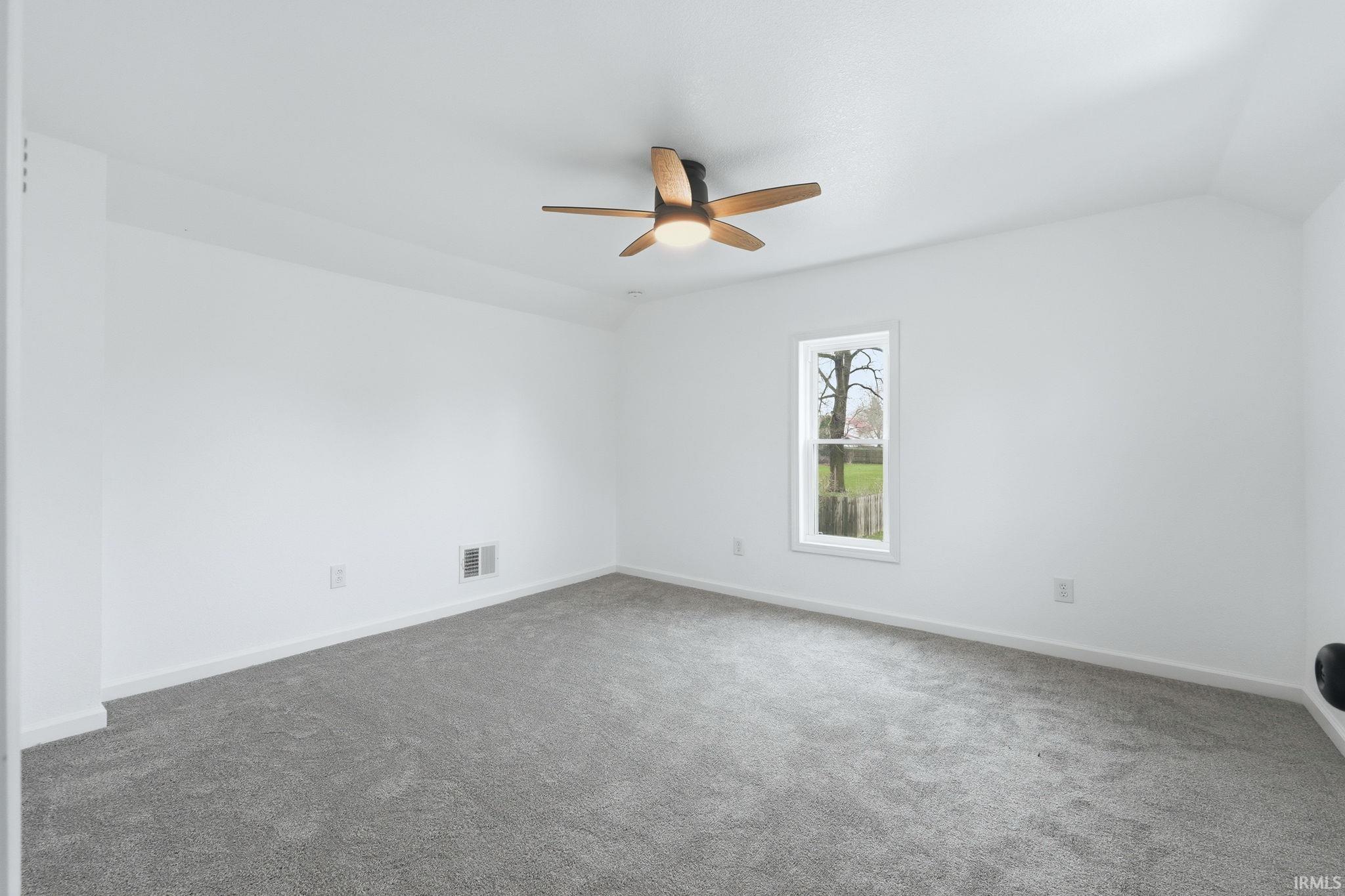 Unfurnished room featuring dark carpet, vaulted ceiling, and ceiling fan