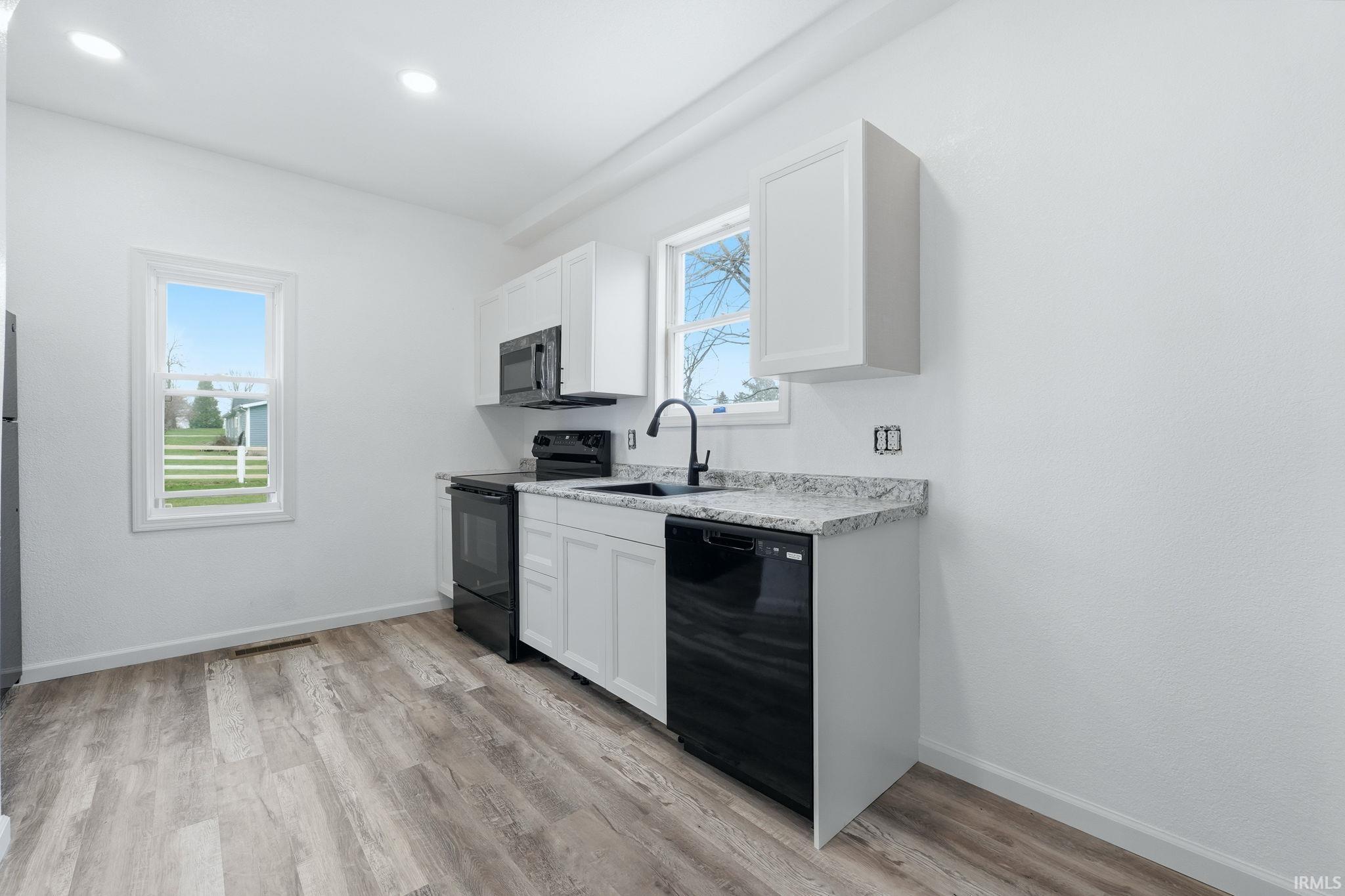 Kitchen featuring black appliances, light countertops, white cabinetry, and light wood-type flooring