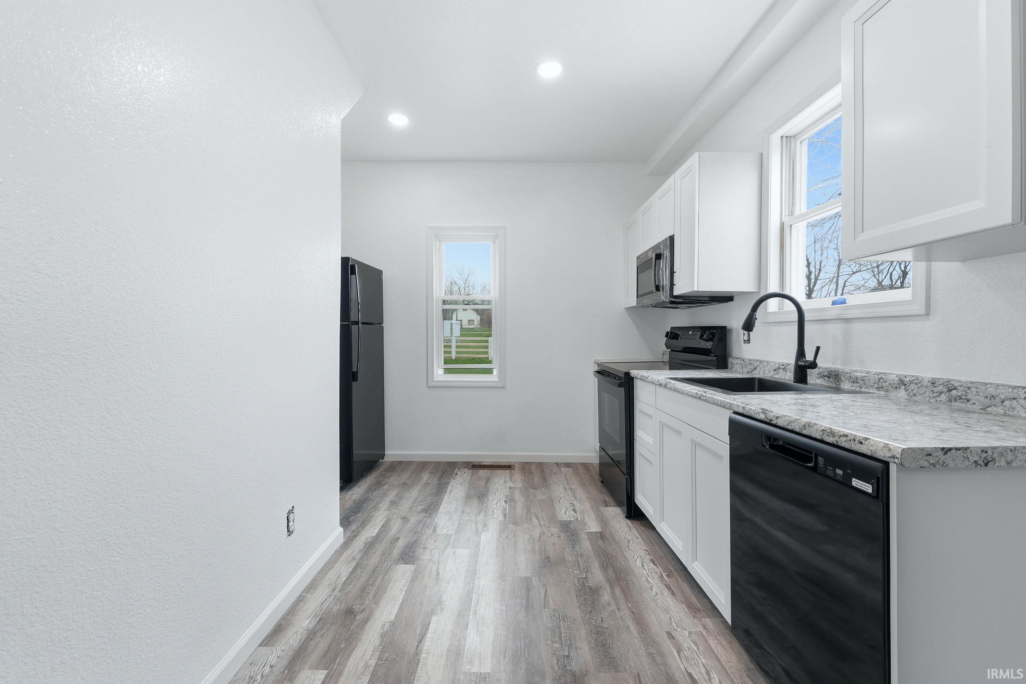 Kitchen featuring black appliances, light countertops, white cabinetry, light wood-type flooring, and recessed lighting