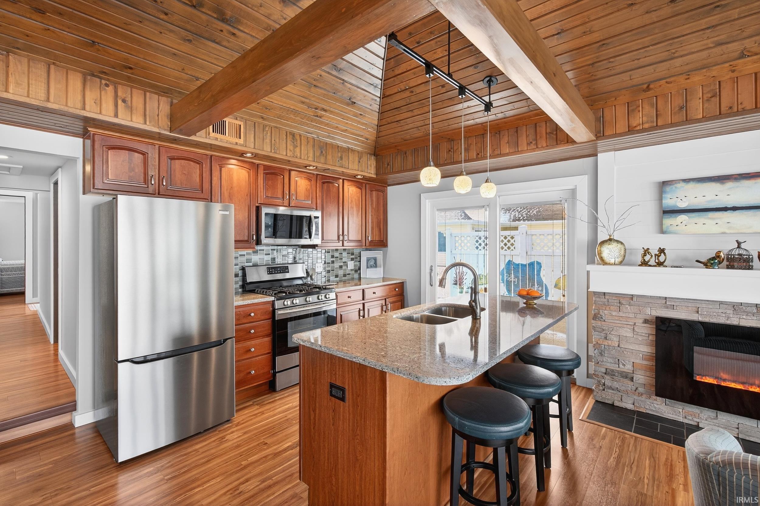 Kitchen featuring a wood ceiling with exposed beams, stainless steel appliances, light stone counters, a breakfast bar, and wood finish cabinetry