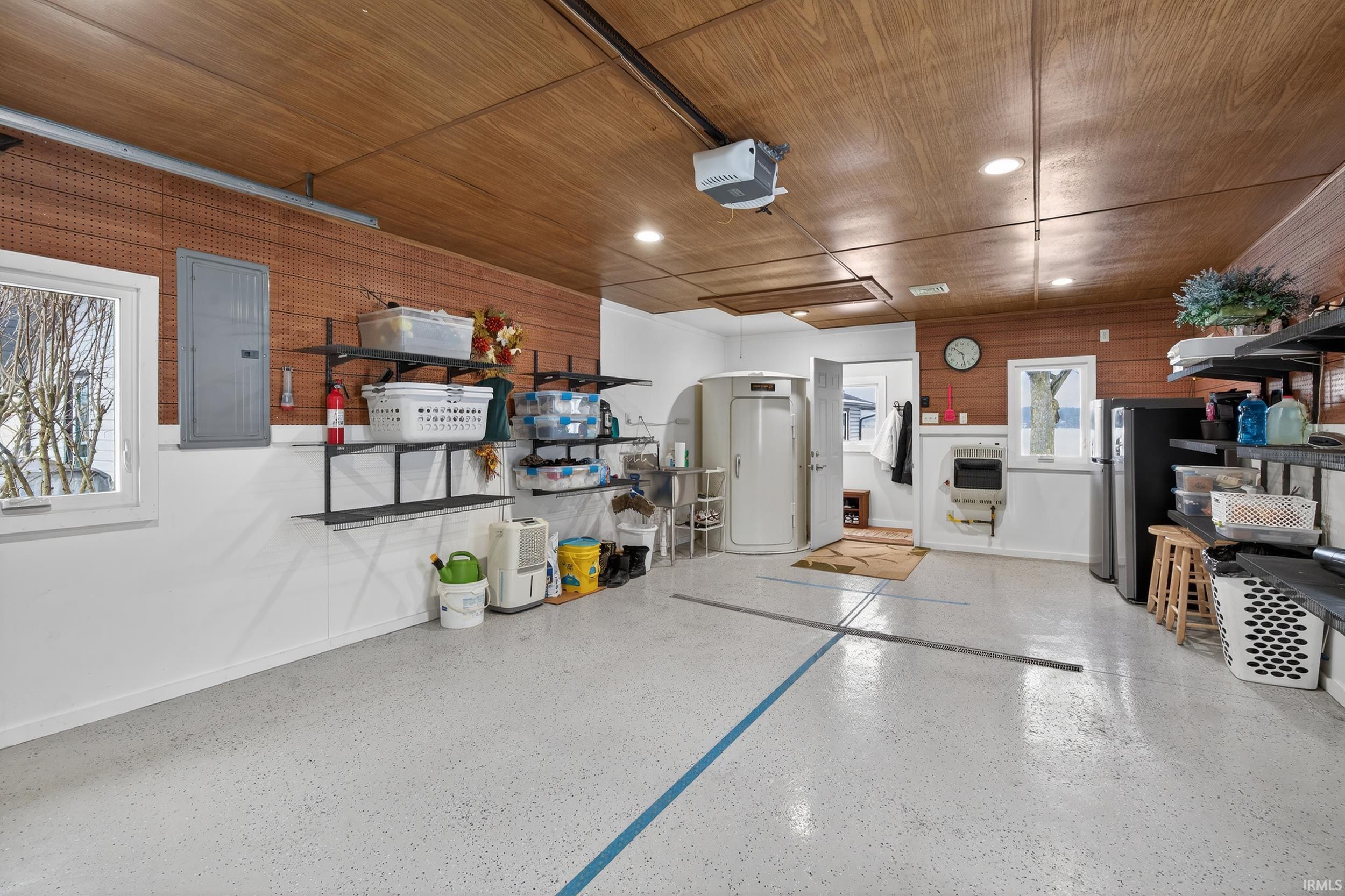 Garage featuring electric panel, wood ceiling, a garage door opener, wooden walls, and freestanding refrigerator