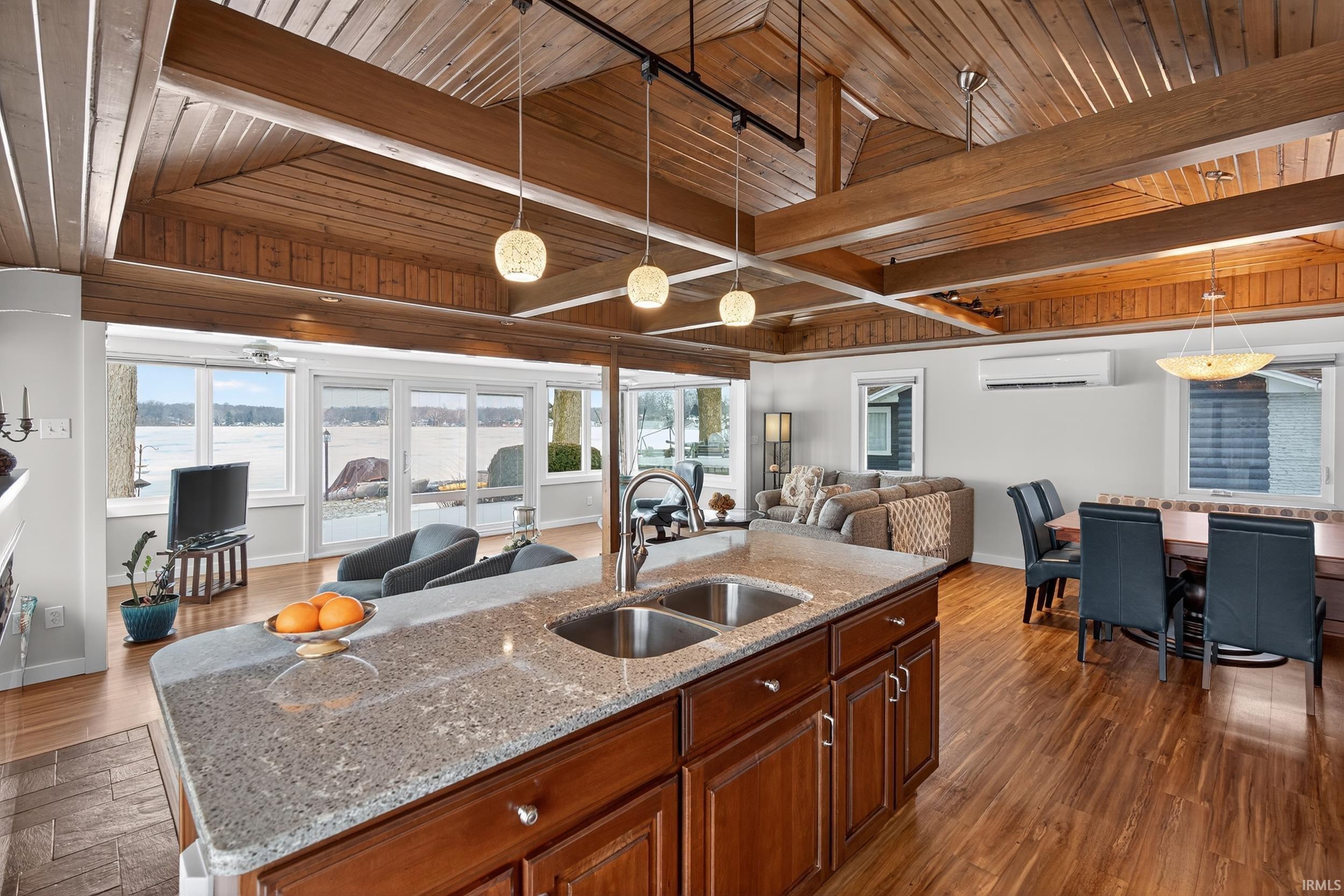 Kitchen featuring open floor plan, a wood ceiling with exposed beams, light stone counters, a center island with sink, and dark wood-type flooring