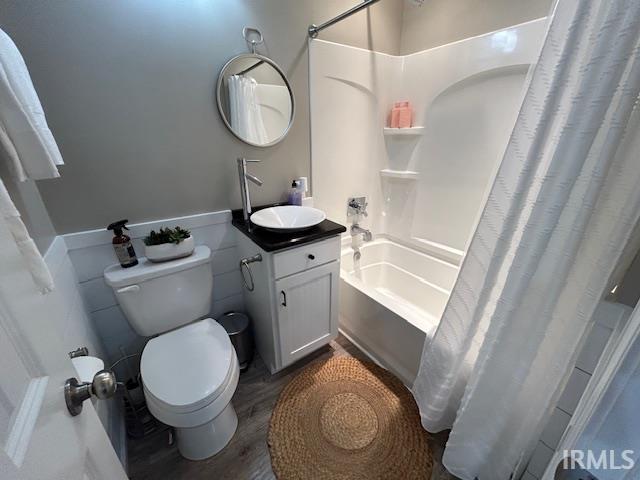 Full bath with vanity, shower / bath combo with shower curtain, dark wood finished floors, and a wainscoted wall