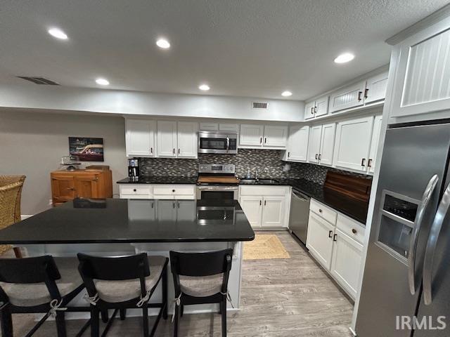 Kitchen with a kitchen breakfast bar, stainless steel appliances, white cabinetry, recessed lighting, and light wood finished floors