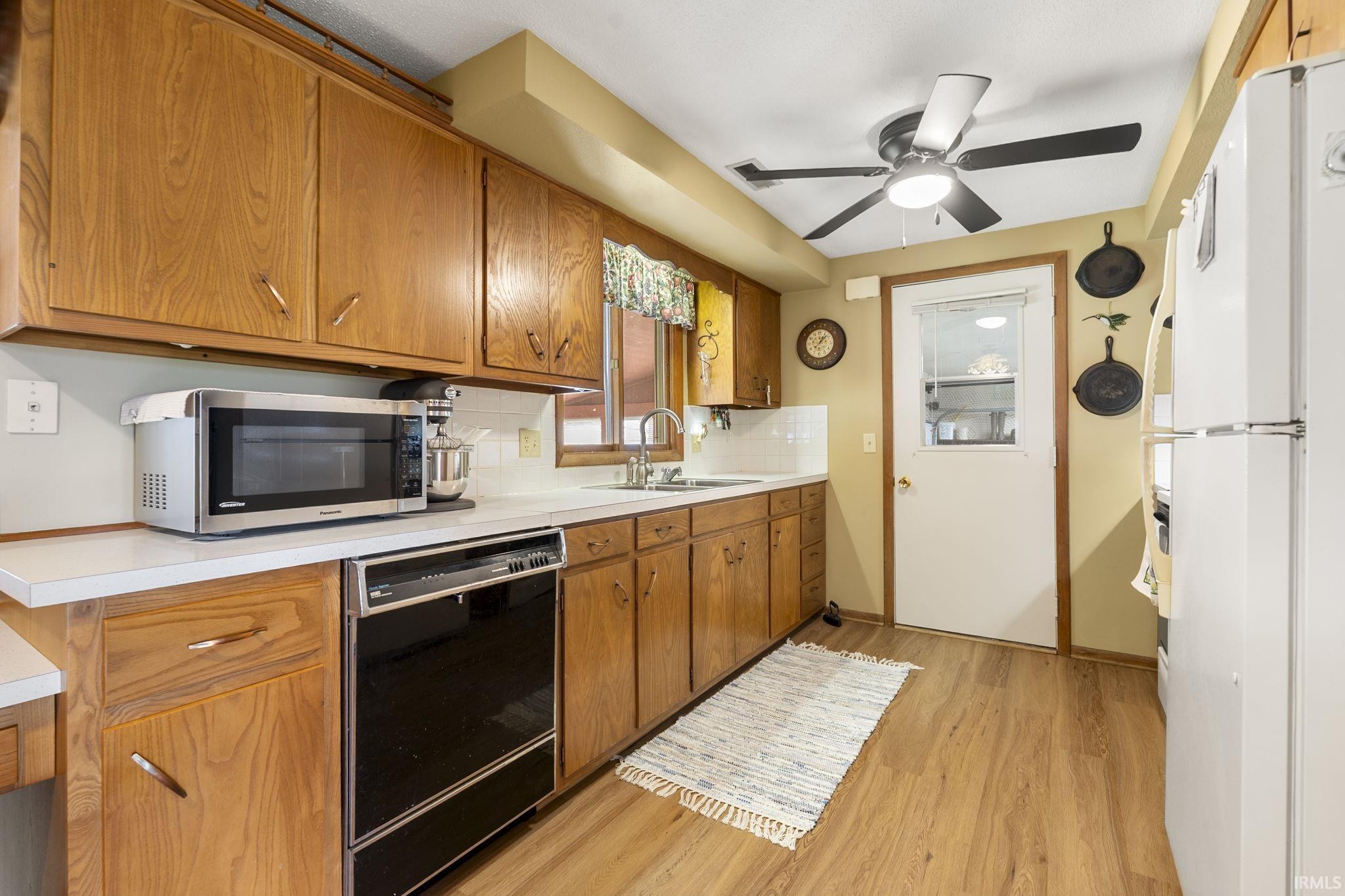 Kitchen featuring wood finish cabinets, dishwasher, freestanding refrigerator, and light countertops