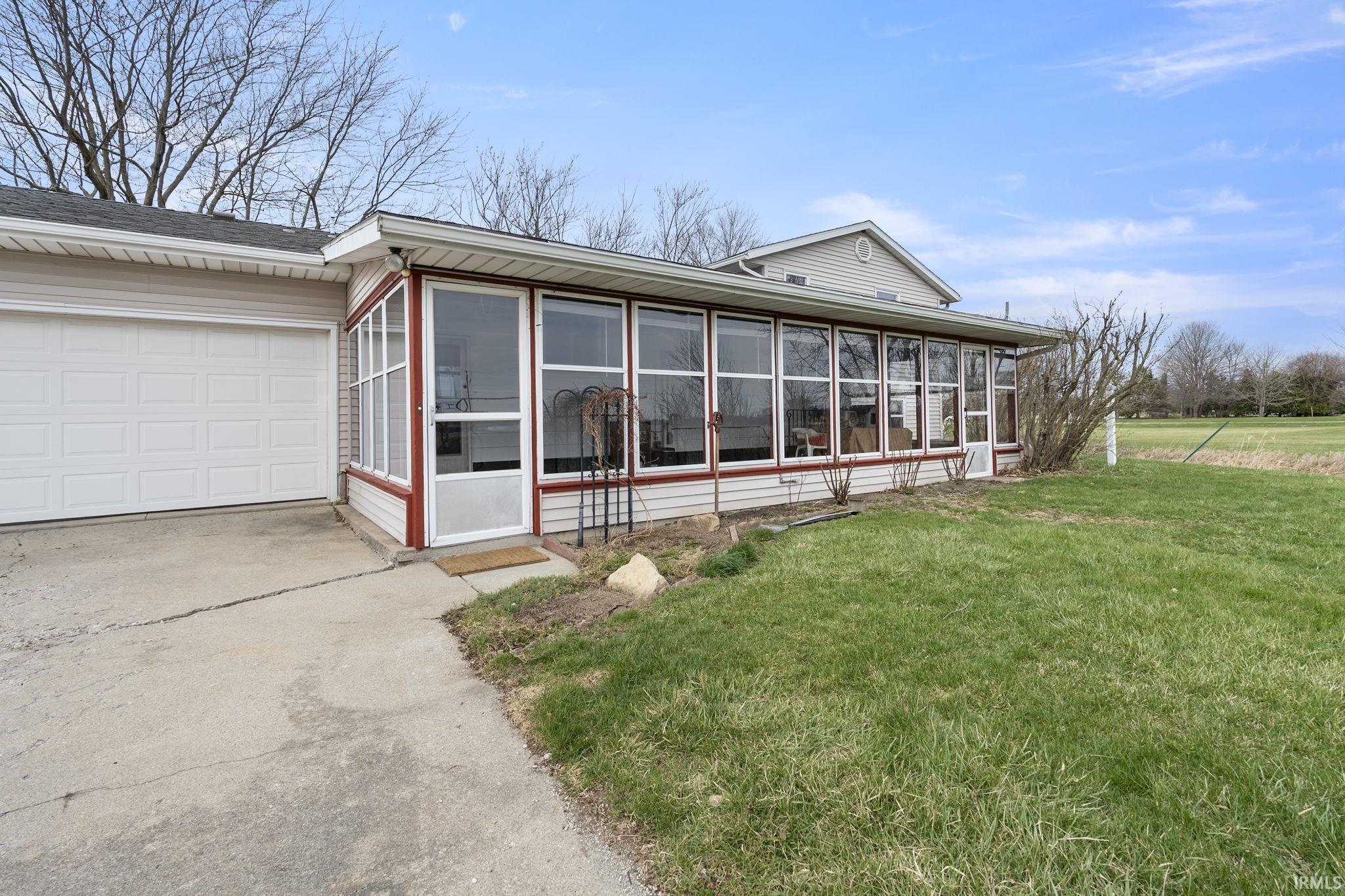 View of property exterior with a yard, driveway, a sunroom, and an attached garage