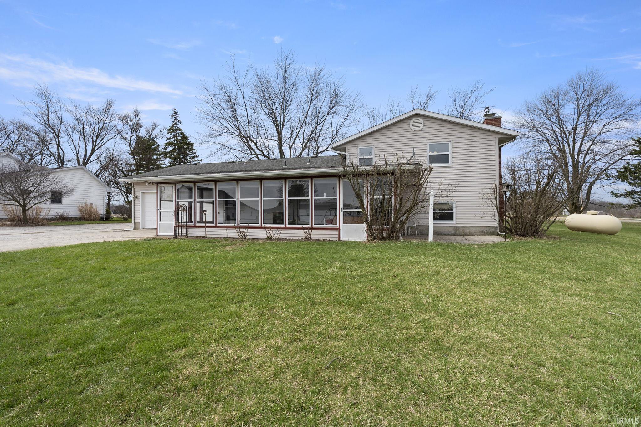 Back of property featuring a sunroom, a yard, a chimney, an attached garage, and driveway