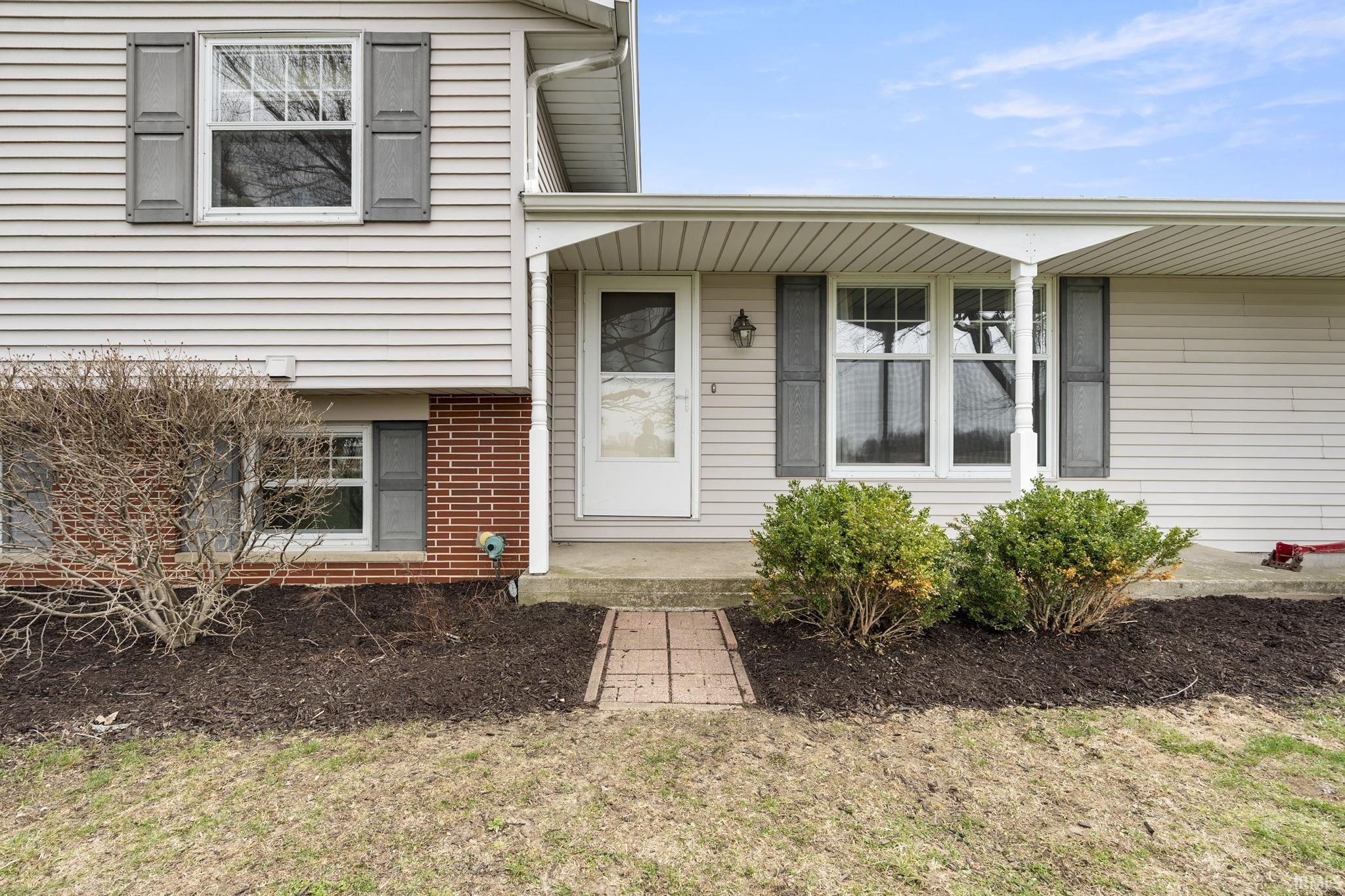 Entrance to property with a porch, a lawn, and brick siding