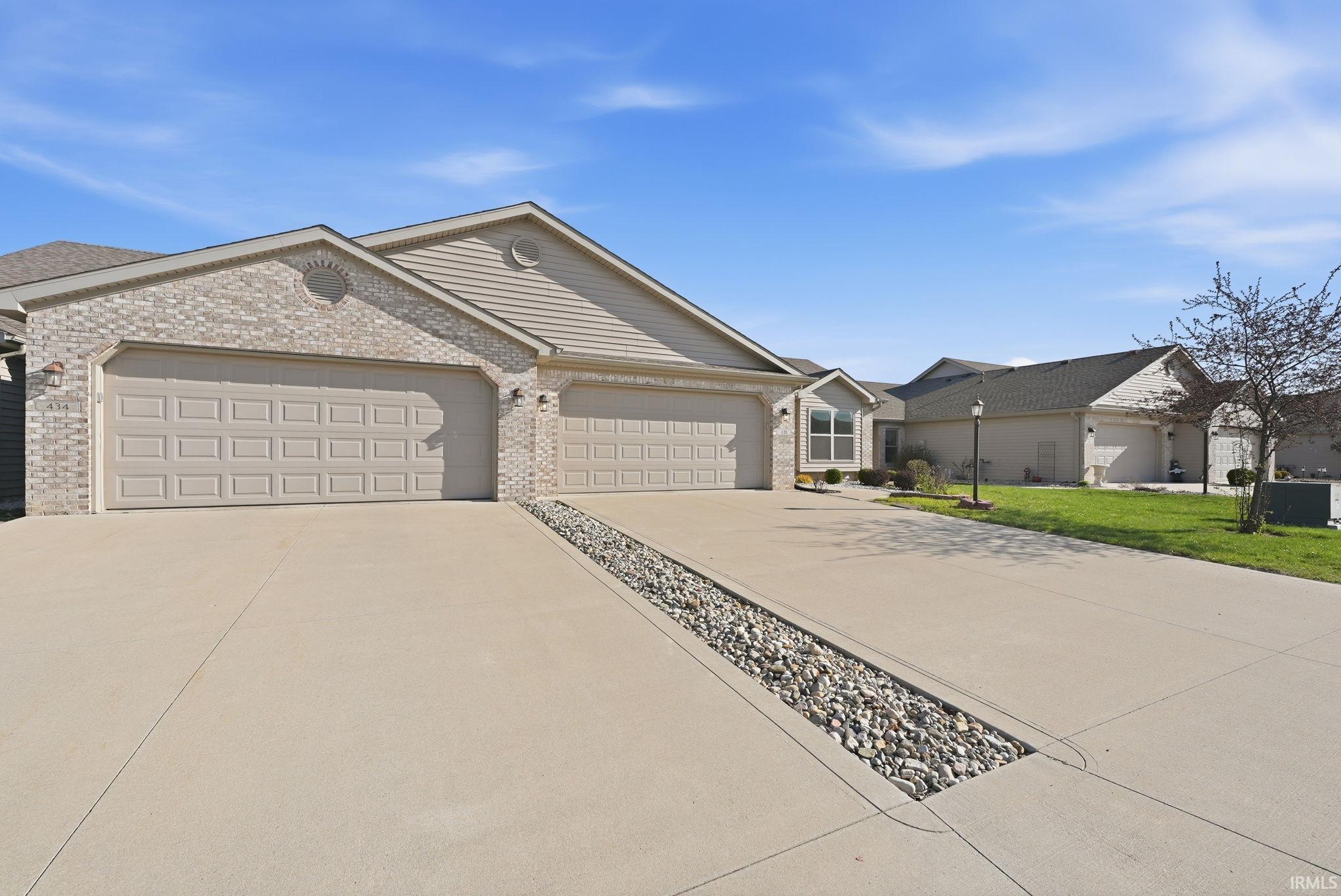 Ranch-style home with driveway, an attached garage, brick siding, and a front yard