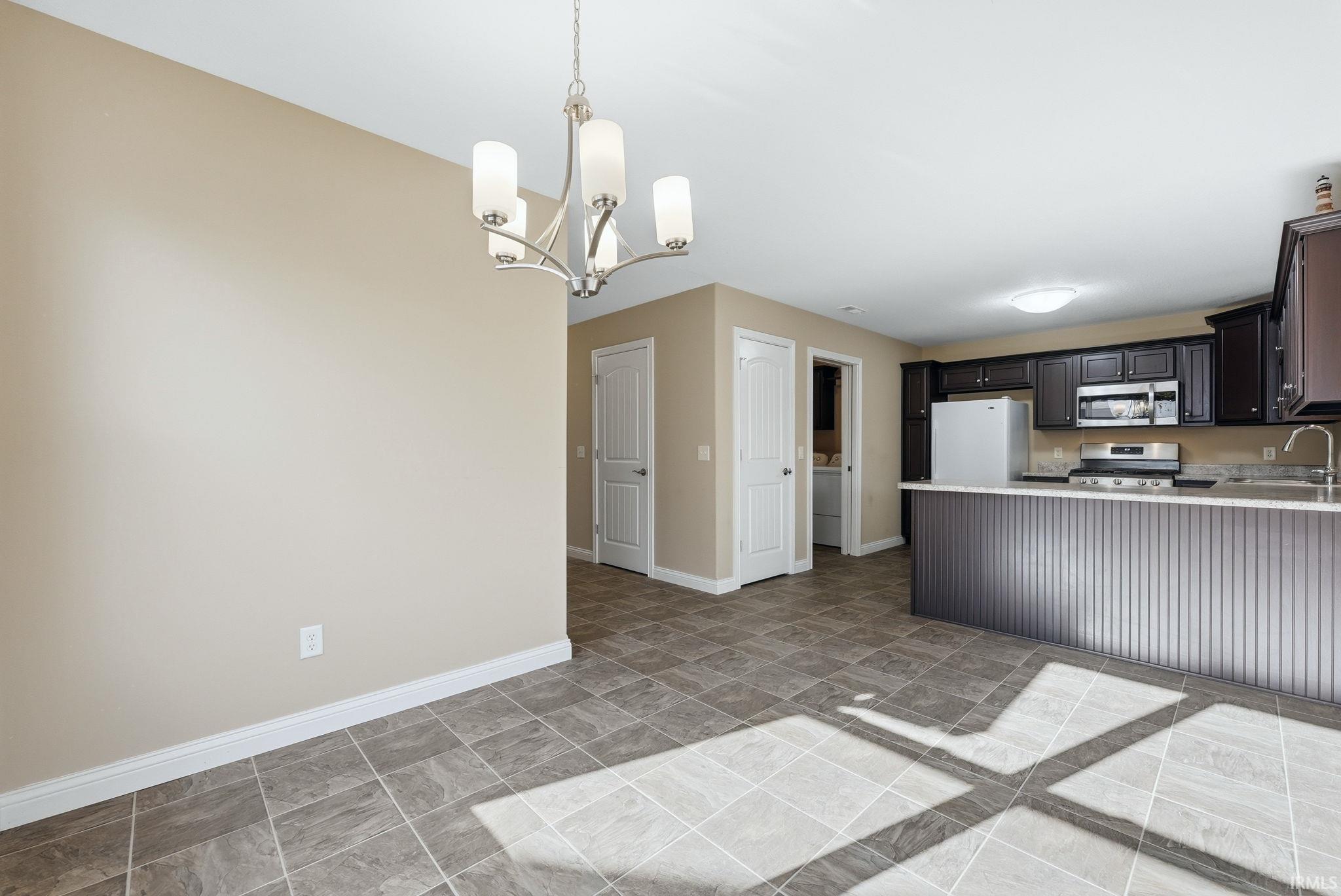 Kitchen with stainless steel appliances, a chandelier, stone finish flooring, a peninsula, and light stone counters
