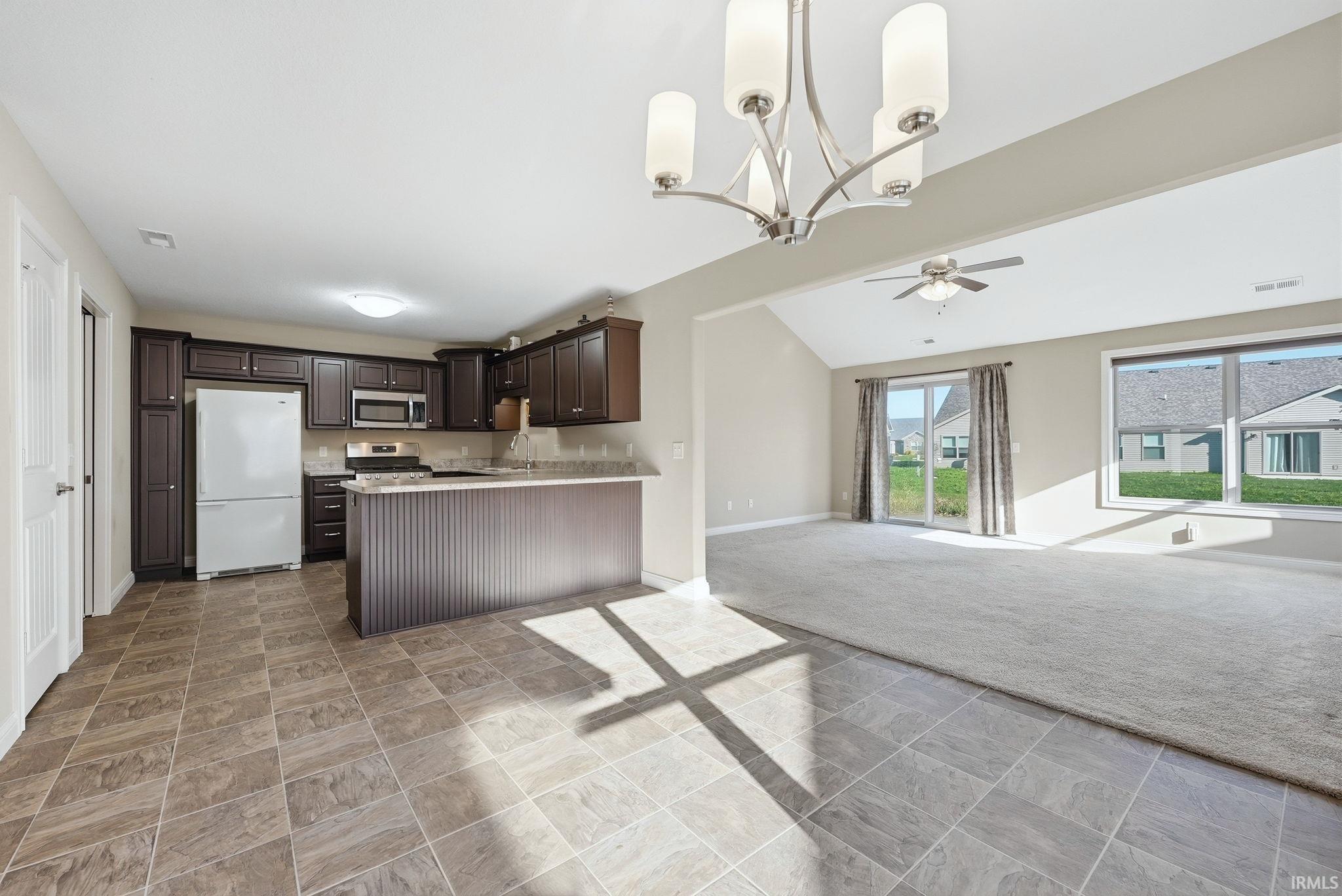 Kitchen with light stone finish floors, open floor plan, stainless steel appliances, a chandelier, and dark wood finish cabinetry