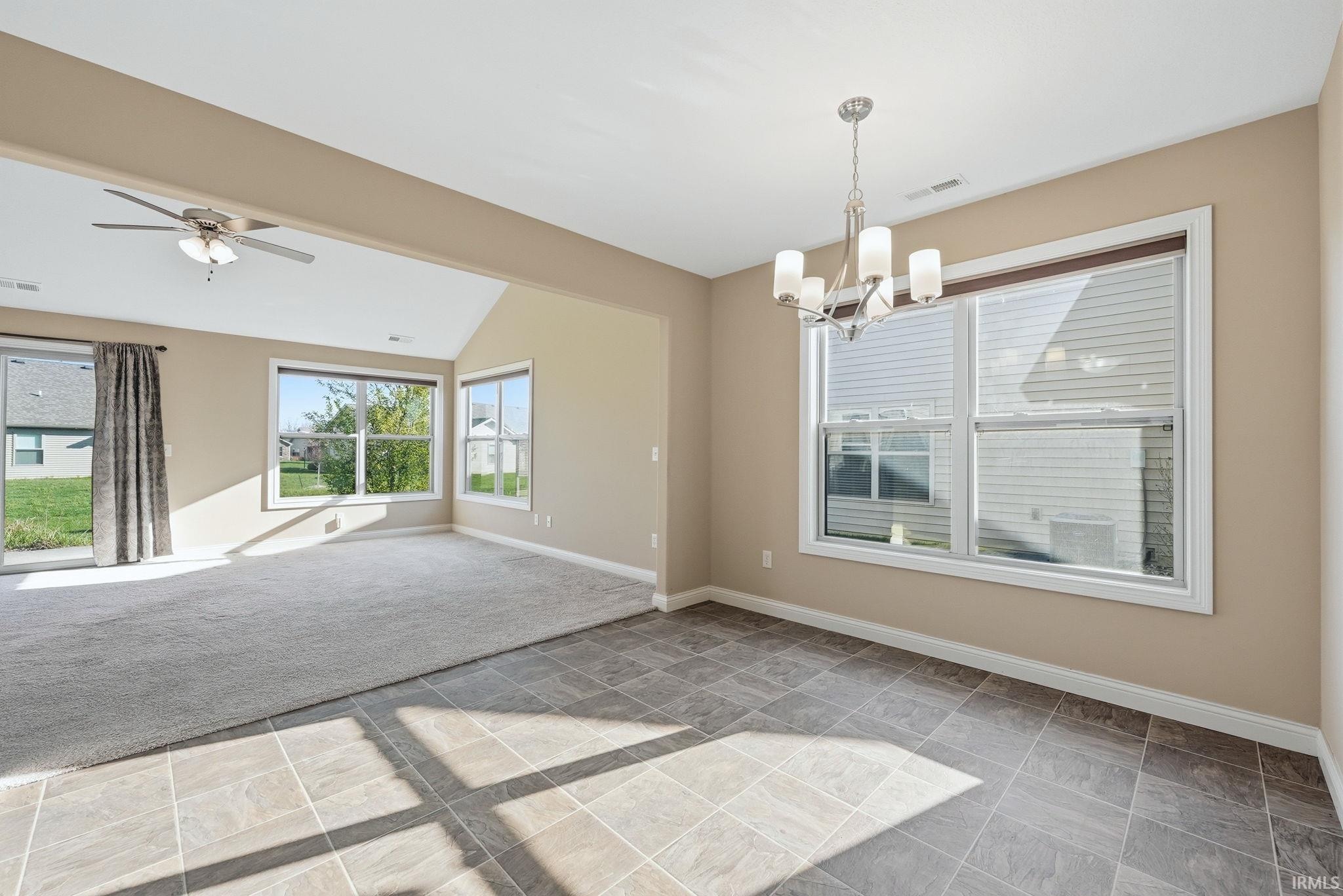 Empty room with stone tile floors, a ceiling fan, a chandelier, and vaulted ceiling