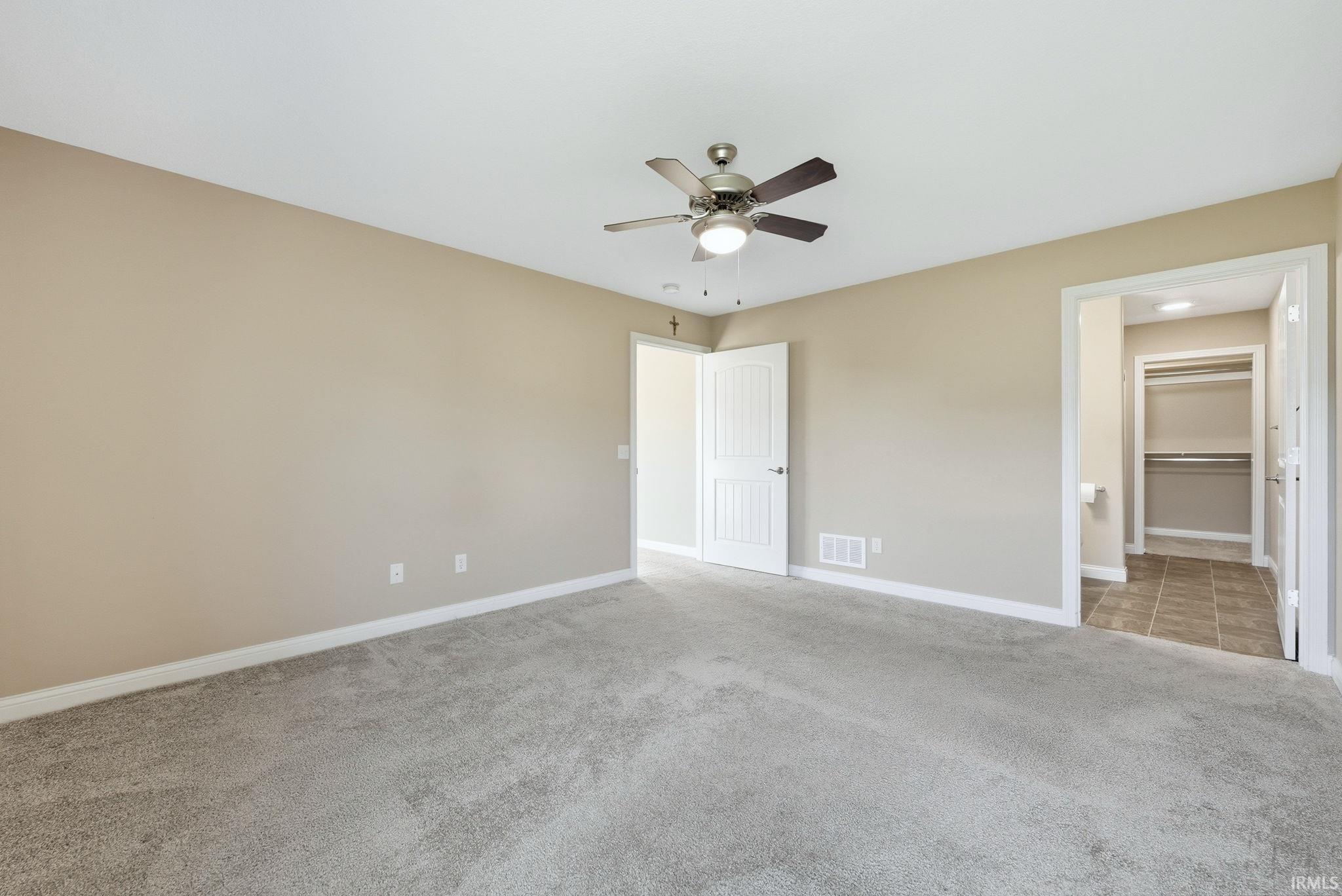 Unfurnished bedroom with light colored carpet, a ceiling fan, and connected bathroom