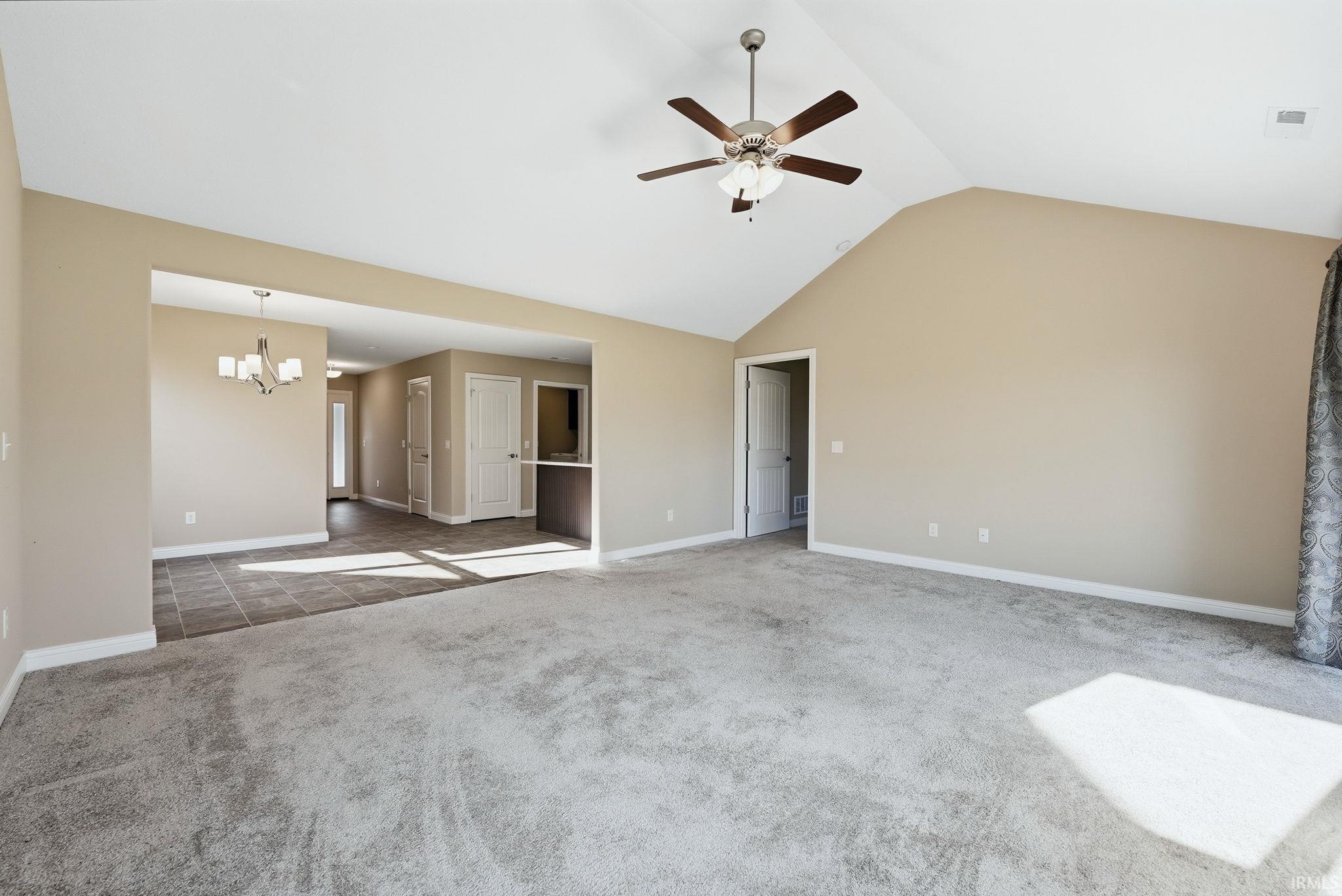 Unfurnished living room featuring a ceiling fan, dark colored carpet, and a chandelier
