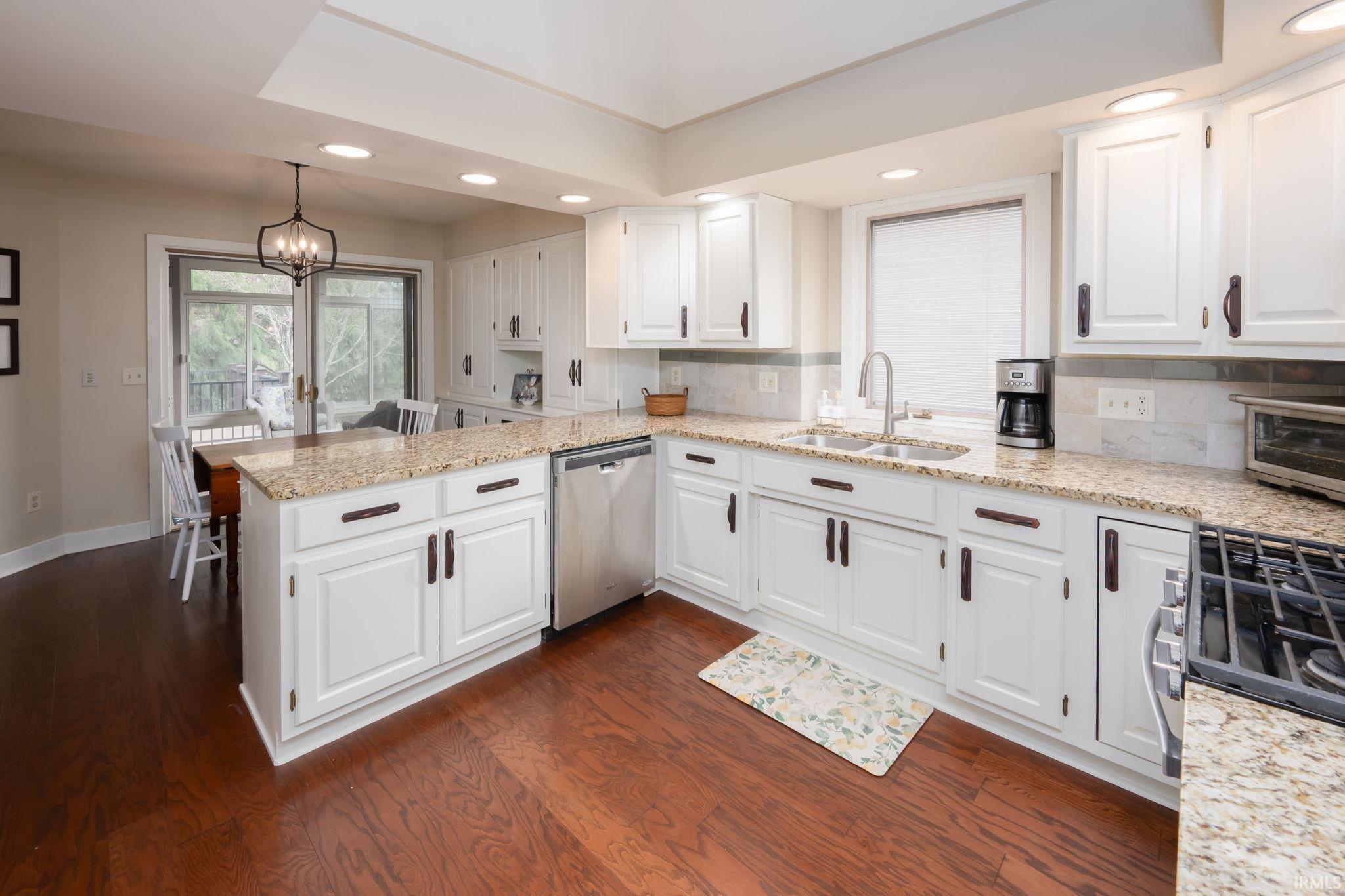 Kitchen featuring a peninsula, light stone counters, white cabinetry, and dishwasher