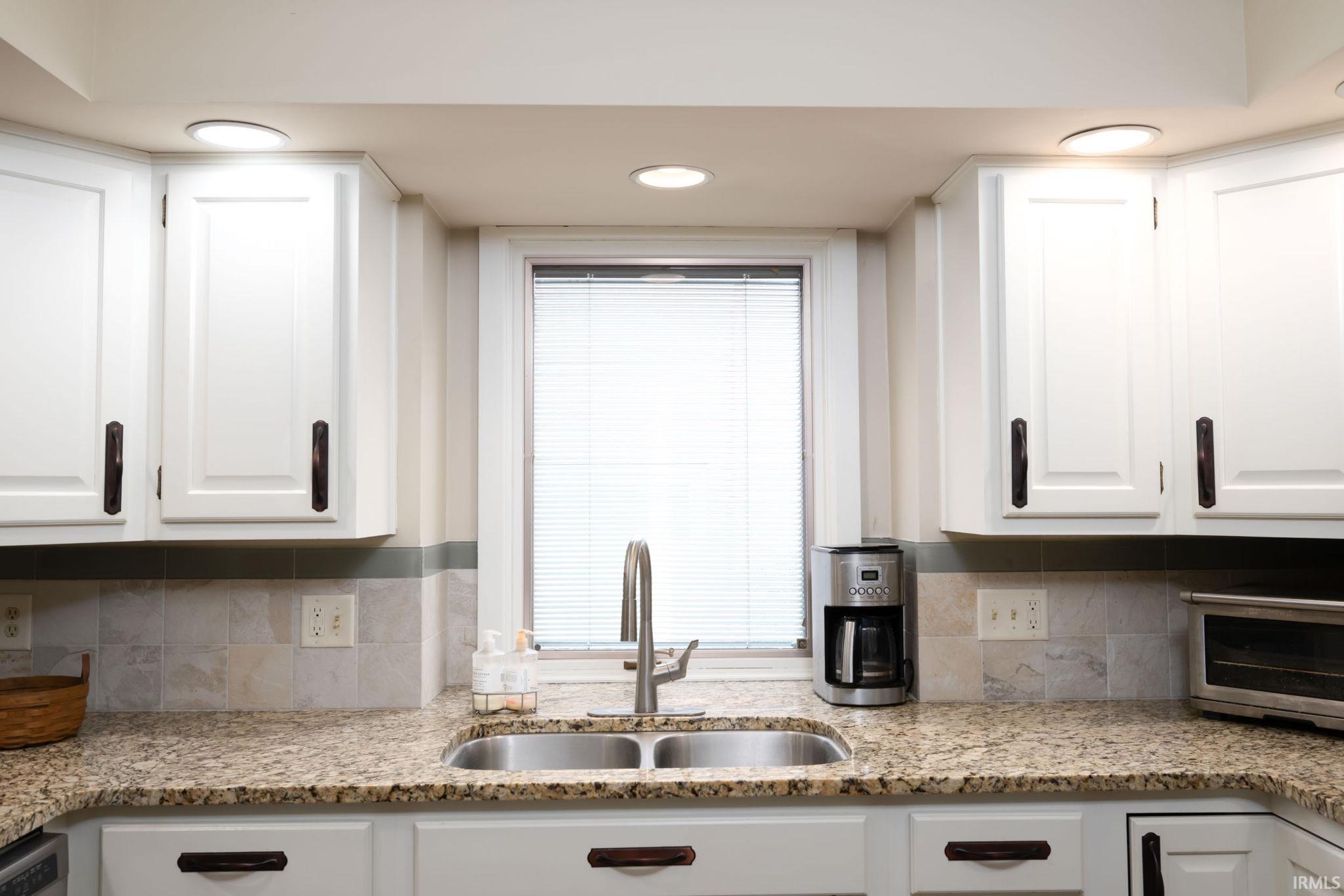 Kitchen featuring white cabinets, light stone counters, tasteful backsplash, and recessed lighting