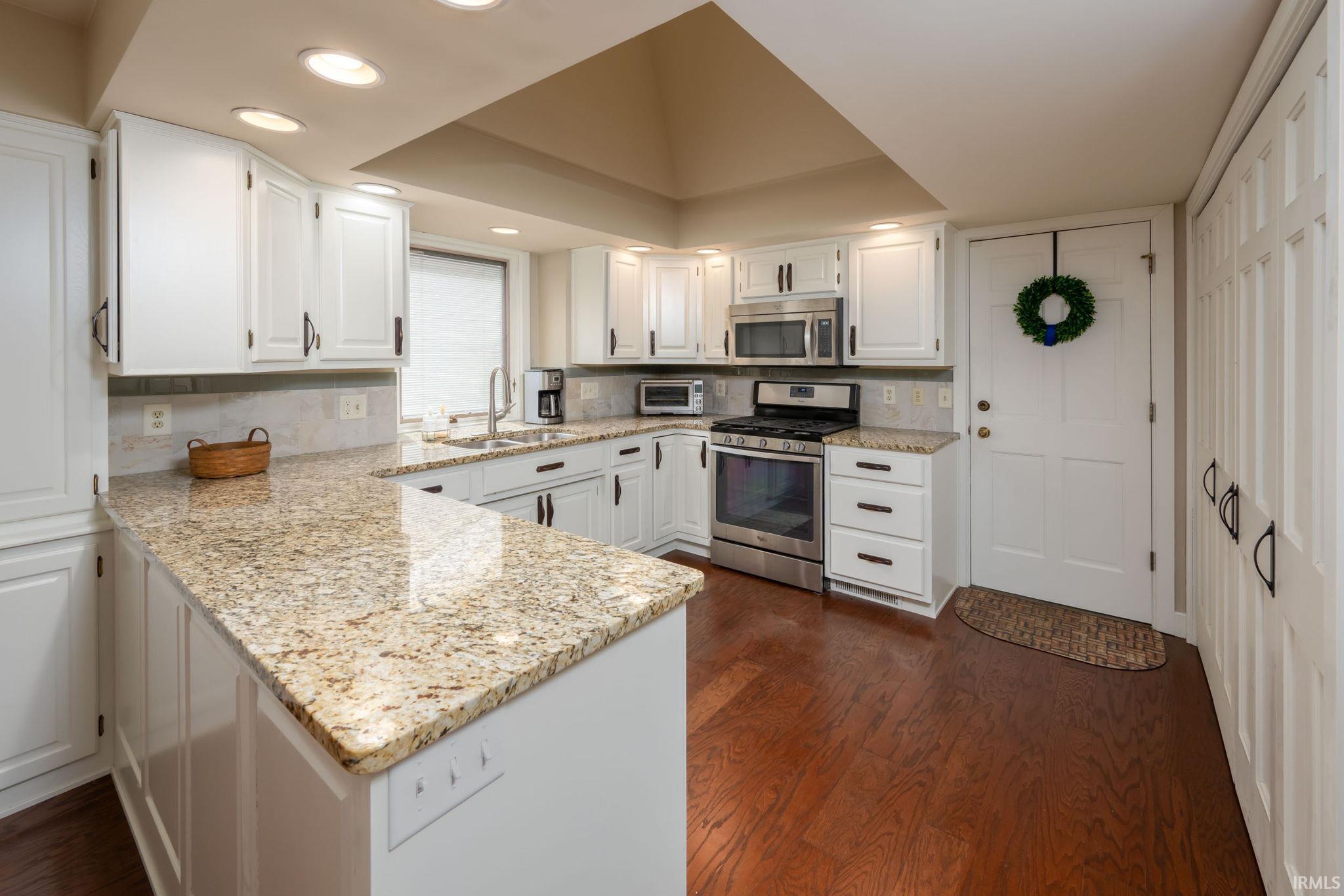 Kitchen with stainless steel appliances, white cabinetry, light stone counters, dark wood-style flooring, and recessed lighting