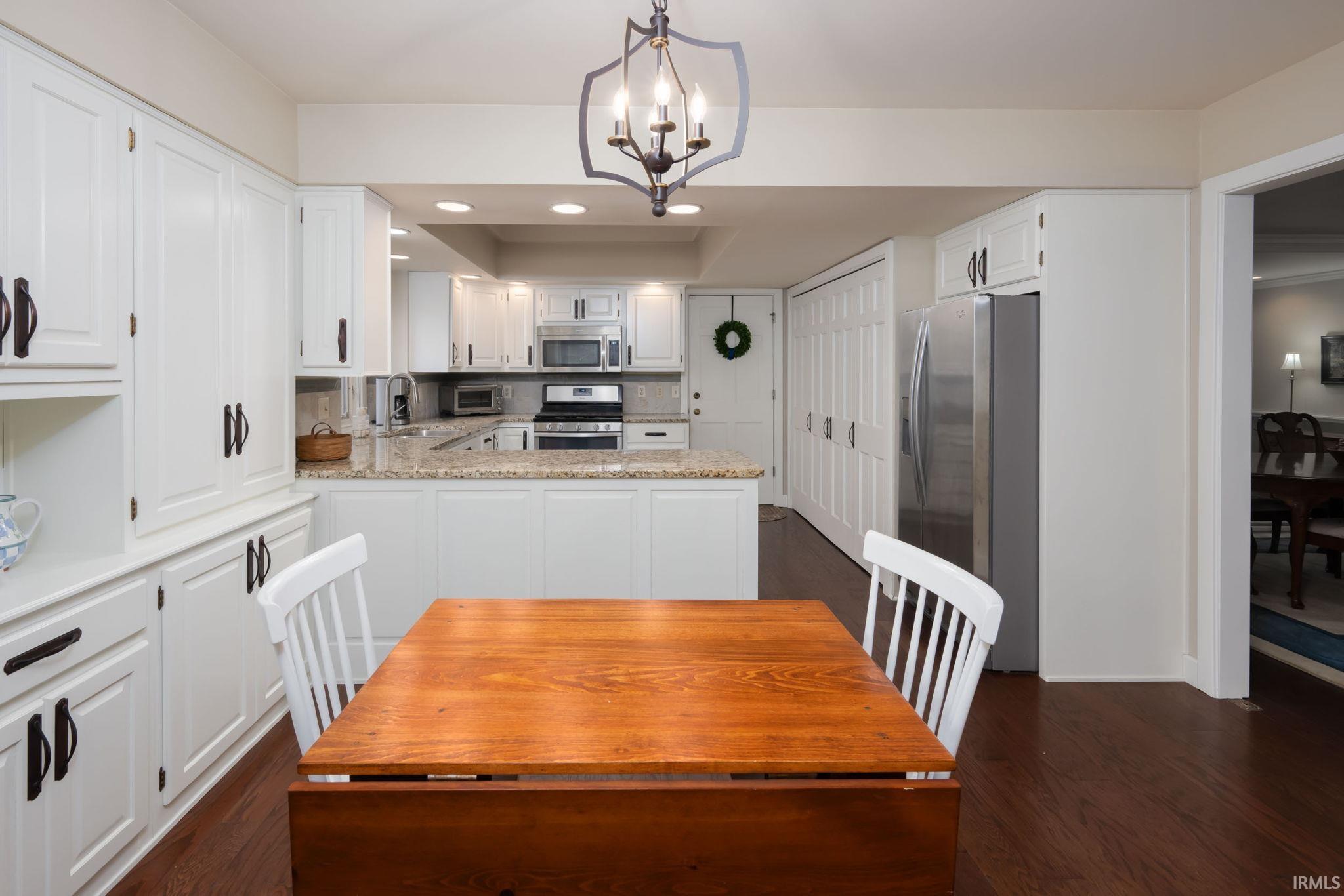 Kitchen featuring stainless steel appliances, white cabinets, suspended lighting, a tray ceiling, and light stone countertops