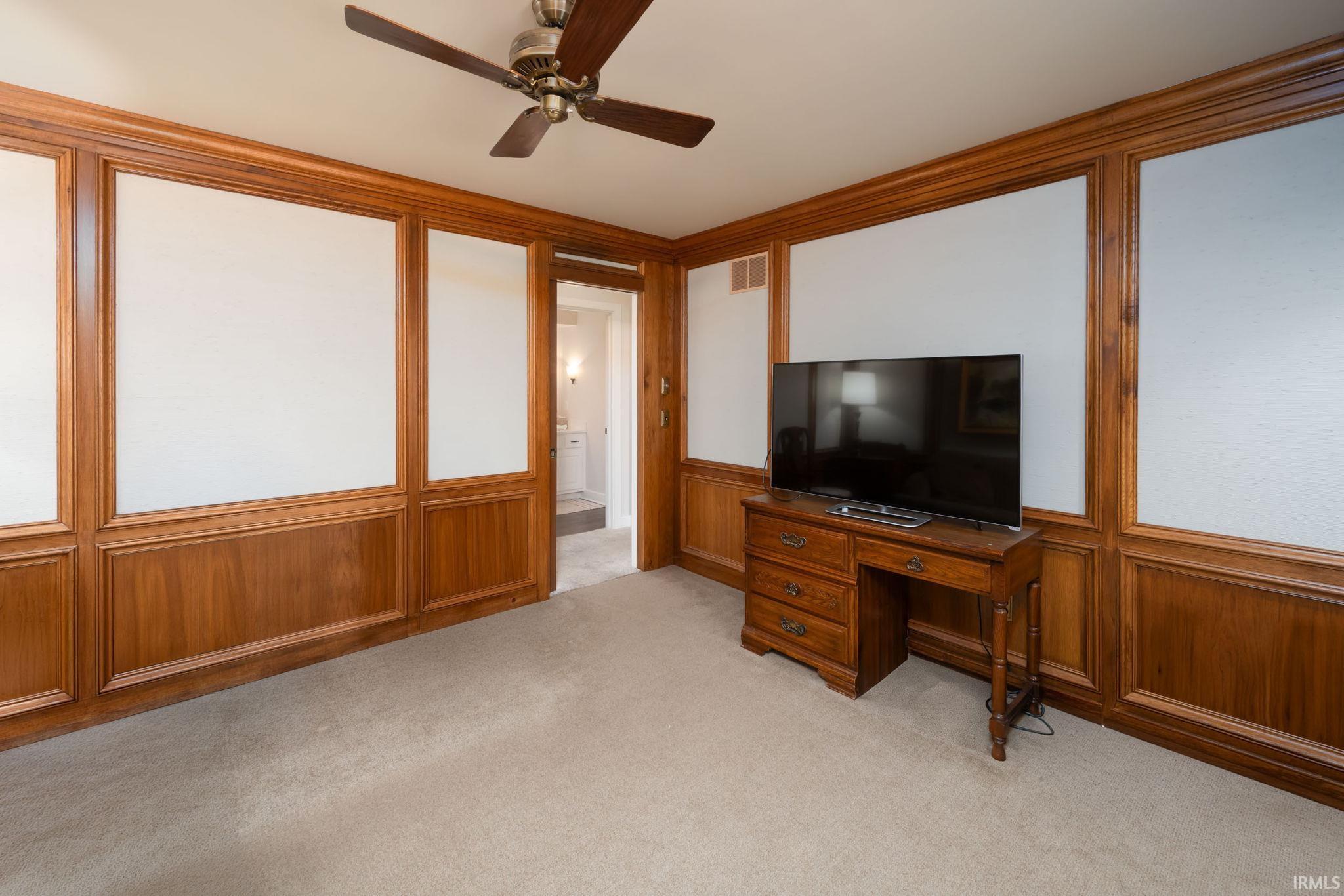 Unfurnished office with a decorative wall, ceiling fan, light carpet, ornamental molding, and wainscoting