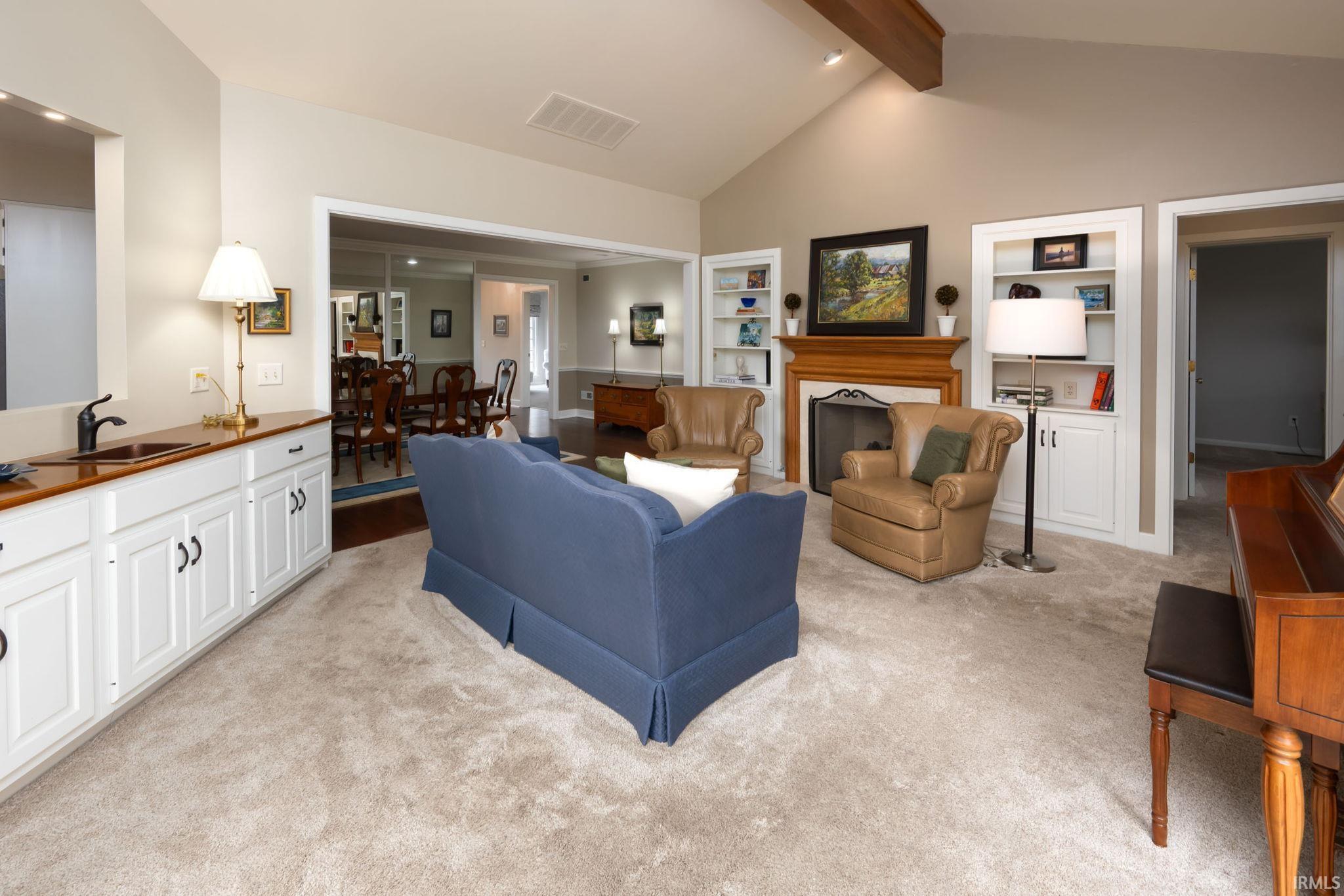 Living room with beam ceiling, built in features, light colored carpet, and a fireplace