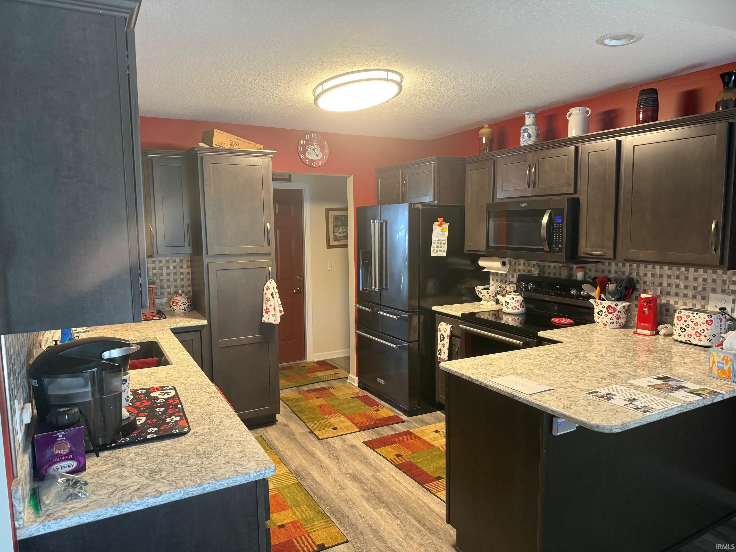 Kitchen featuring electric stove, tasteful backsplash, stainless steel microwave, dark wood finish cabinetry, and light wood-type flooring