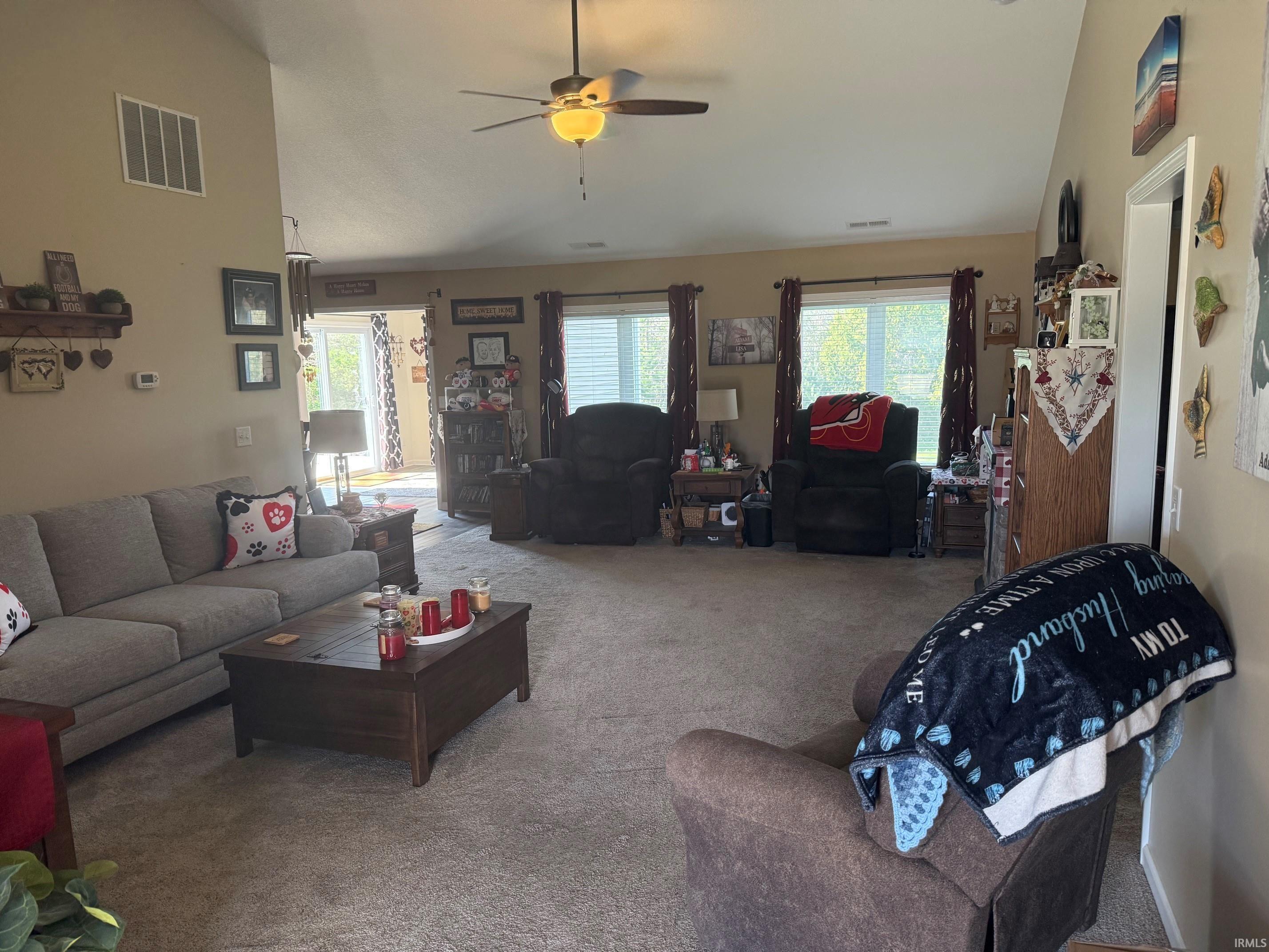 Living area with vaulted ceiling, carpet floors, a ceiling fan, and plenty of natural light