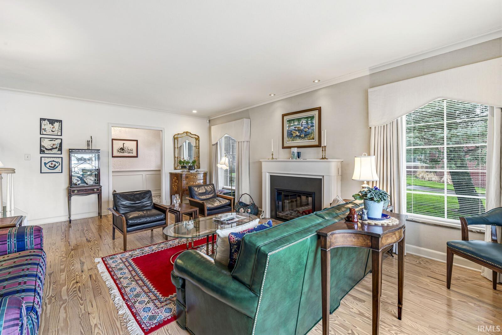 Living room with light wood-type flooring, crown molding, and a glass covered fireplace