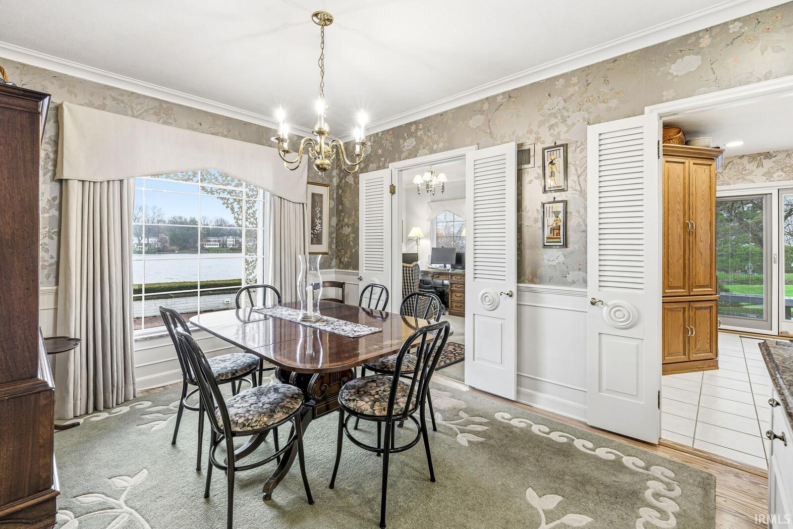 Dining room with wainscoting, wallpapered walls, suspended lighting, crown molding, and a decorative wall