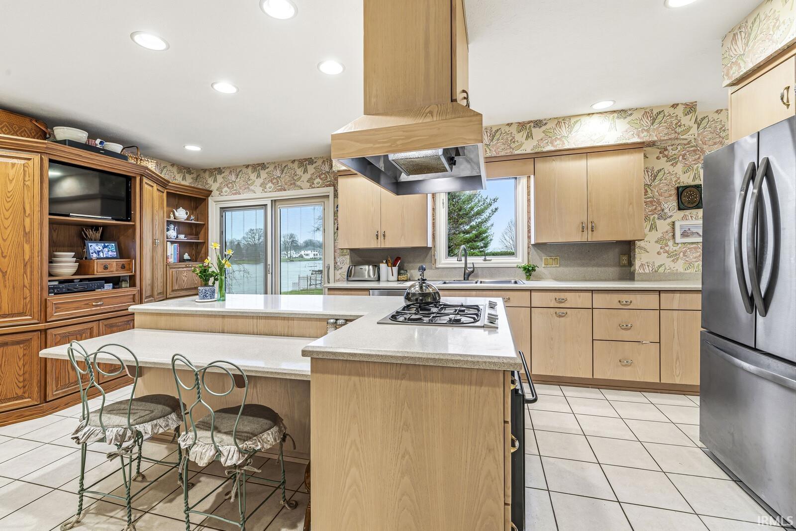 Kitchen with light tile patterned floors, stainless steel appliances, a breakfast bar area, wallpapered walls, and light wood finish cabinets