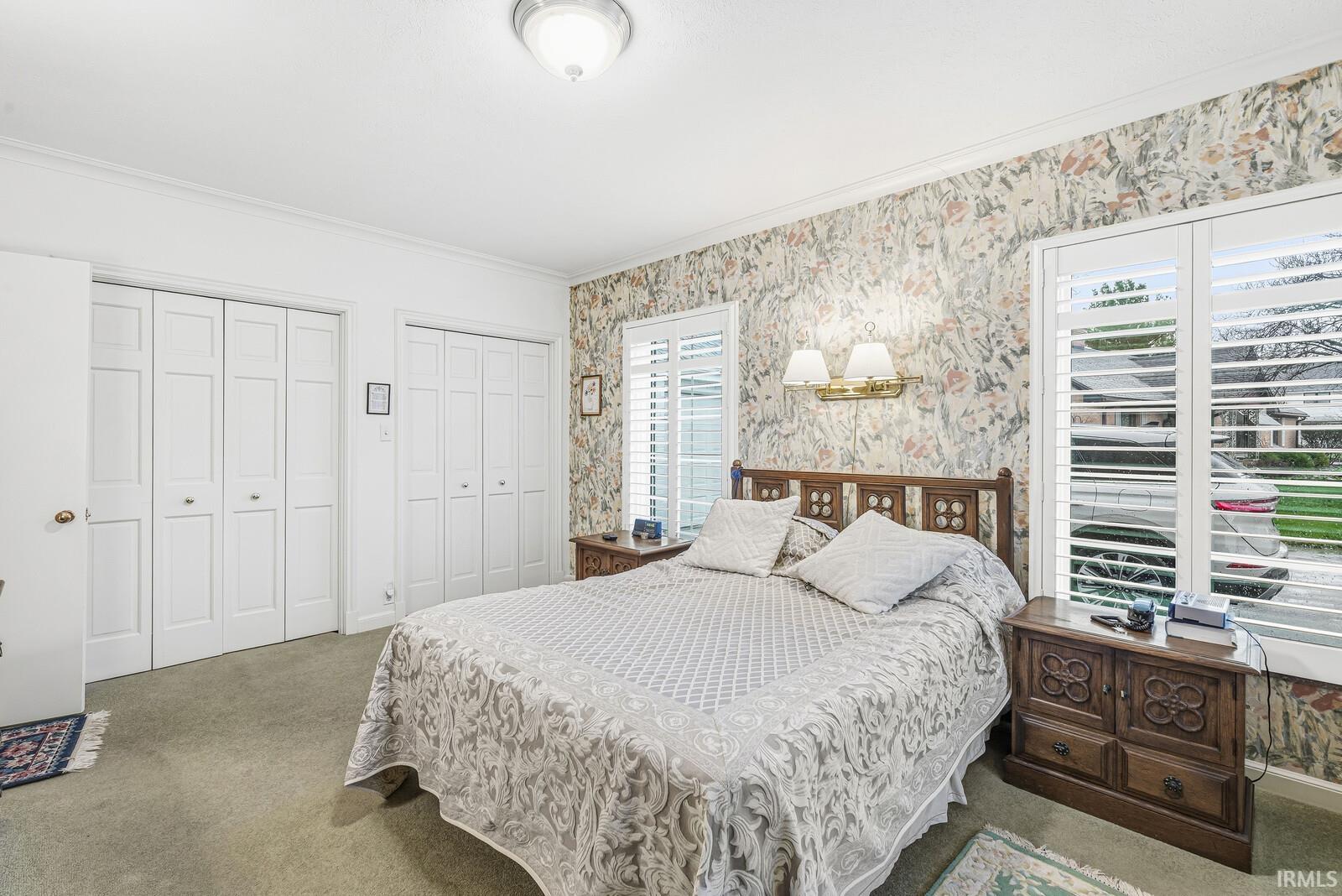 Bedroom with ornamental molding, wallpapered walls, multiple closets, and carpet flooring